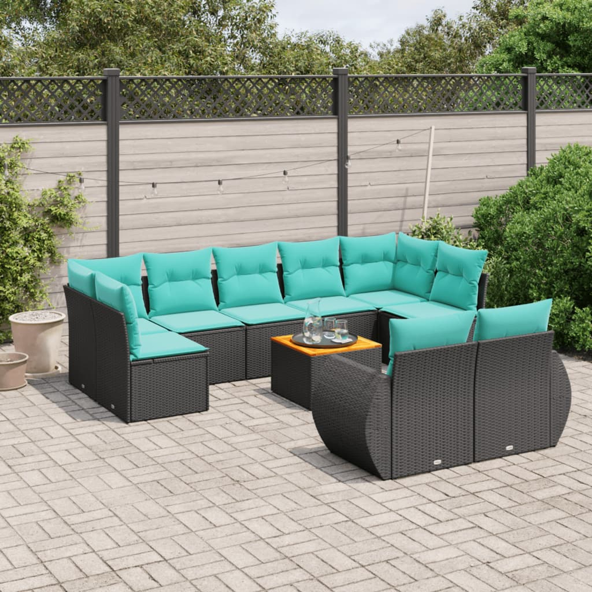 Sofá seccional exterior con cojines turquesa y una mesa pequeña con vasos en un patio. Fondo con valla y vegetación.