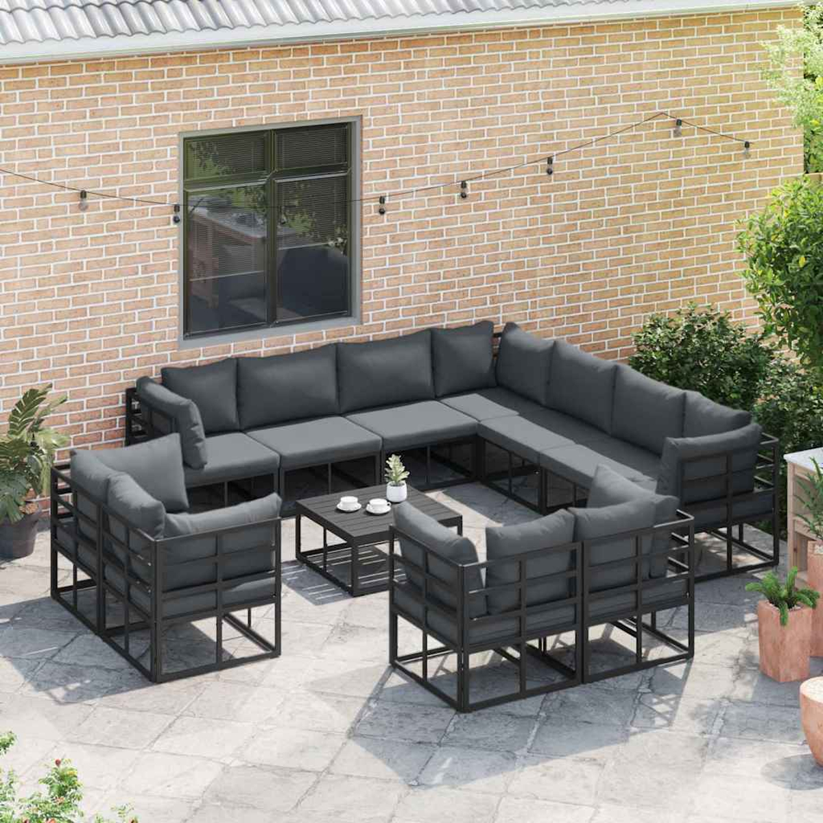 Garten-Set. Graue Kissen auf dunklen Metallrahmen. Couchtisch mit Pflanzen. Backsteinmauer im Hintergrund mit Fenster.