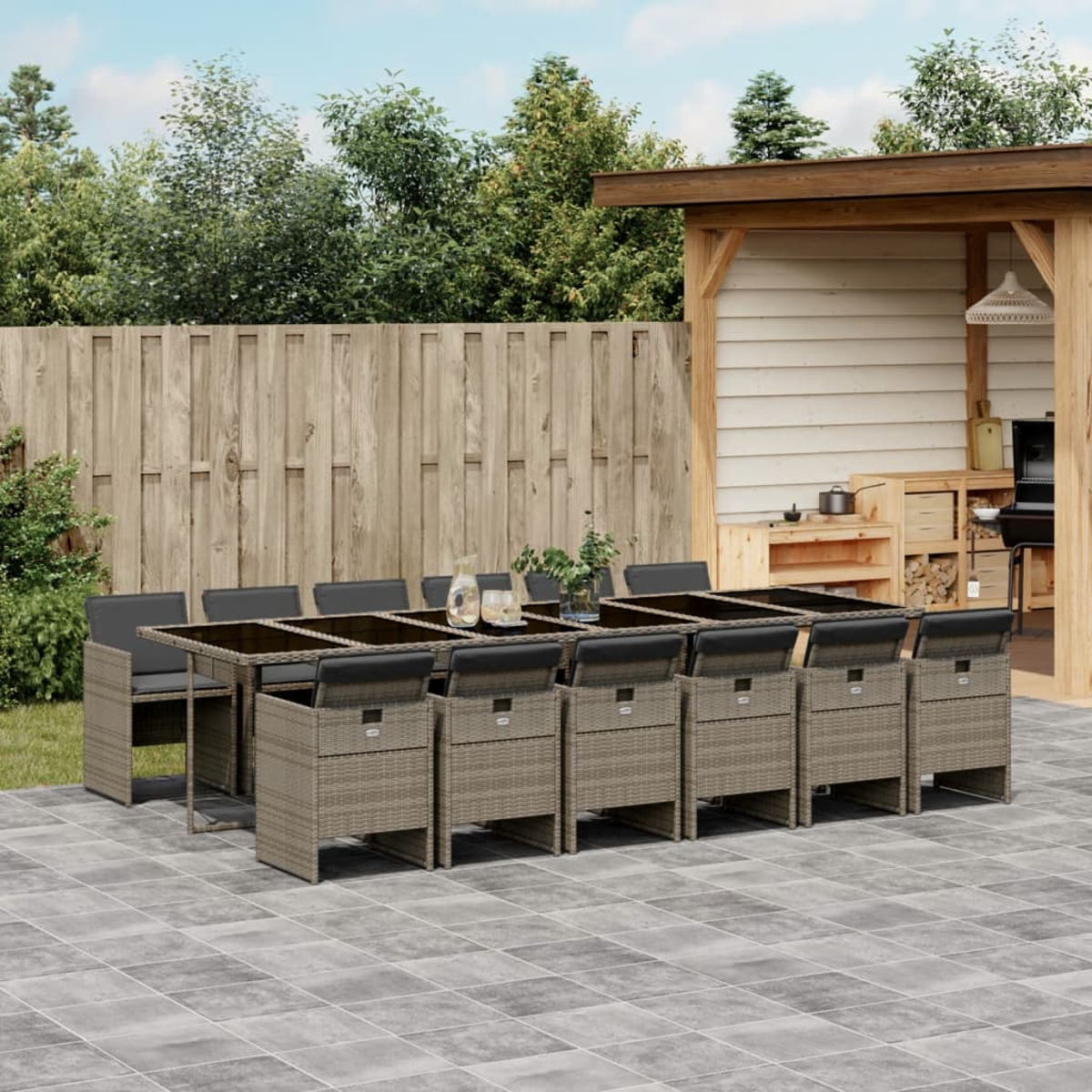 Juego de comedor al aire libre con mesa y sillas. Valla de madera y árboles al fondo. Zona de patio con cocina.