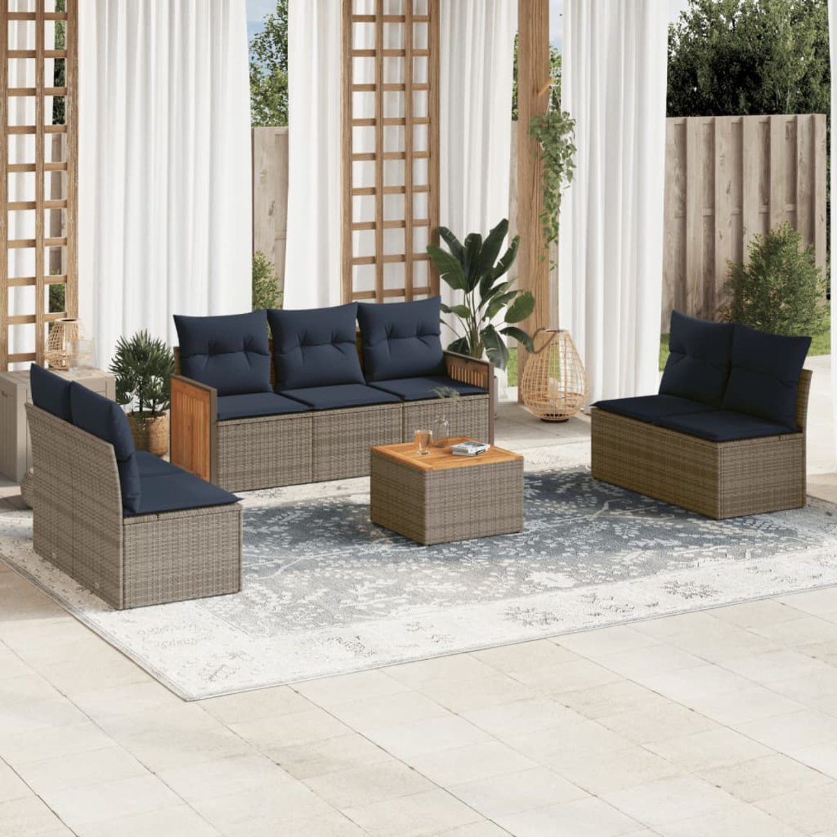 Terrassenset mit Sofa, Sesseln und Couchtisch auf einem Teppich. Dunkelblaue Kissen, hellbraune Korbmöbel und weiße Vorhänge.