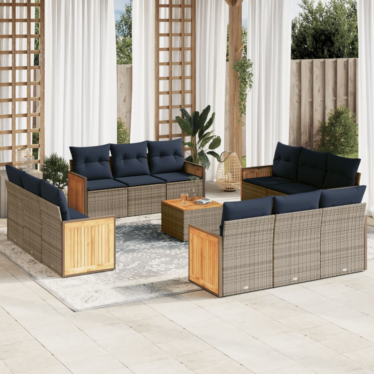 Garten-Set mit grauem Korbmöbeln, marinefarbenen Kissen und einem Holztisch. Weiße Vorhänge und Pflanzen im Hintergrund.