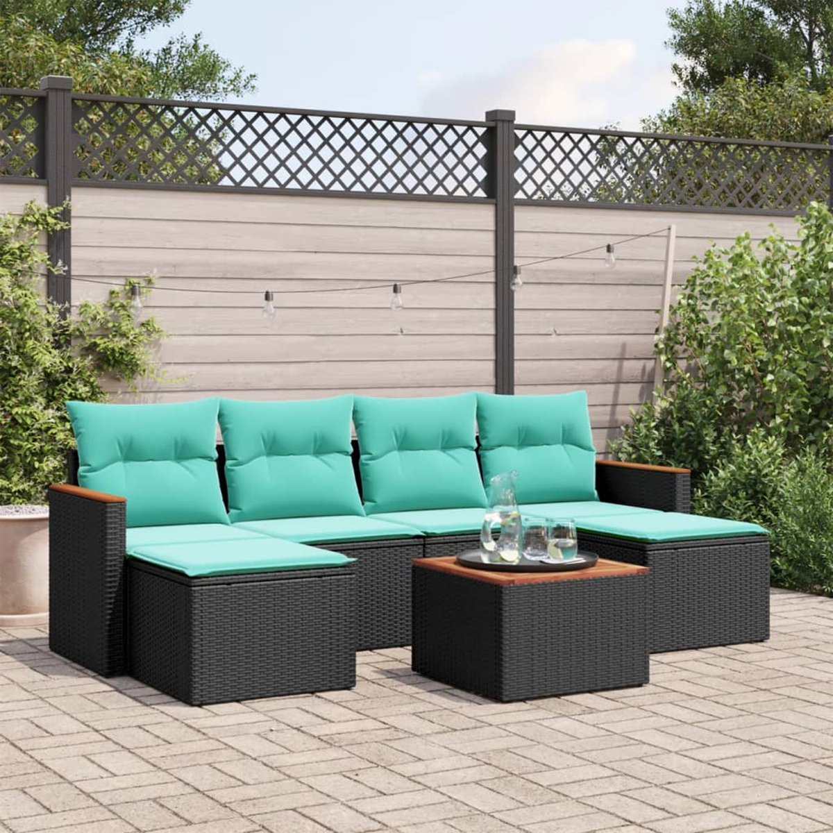 Garten-Sitzgruppe mit türkisfarbenen Kissen und einem Holztisch auf einer Ziegelterrasse, mit Zaun und Grün im Hintergrund.