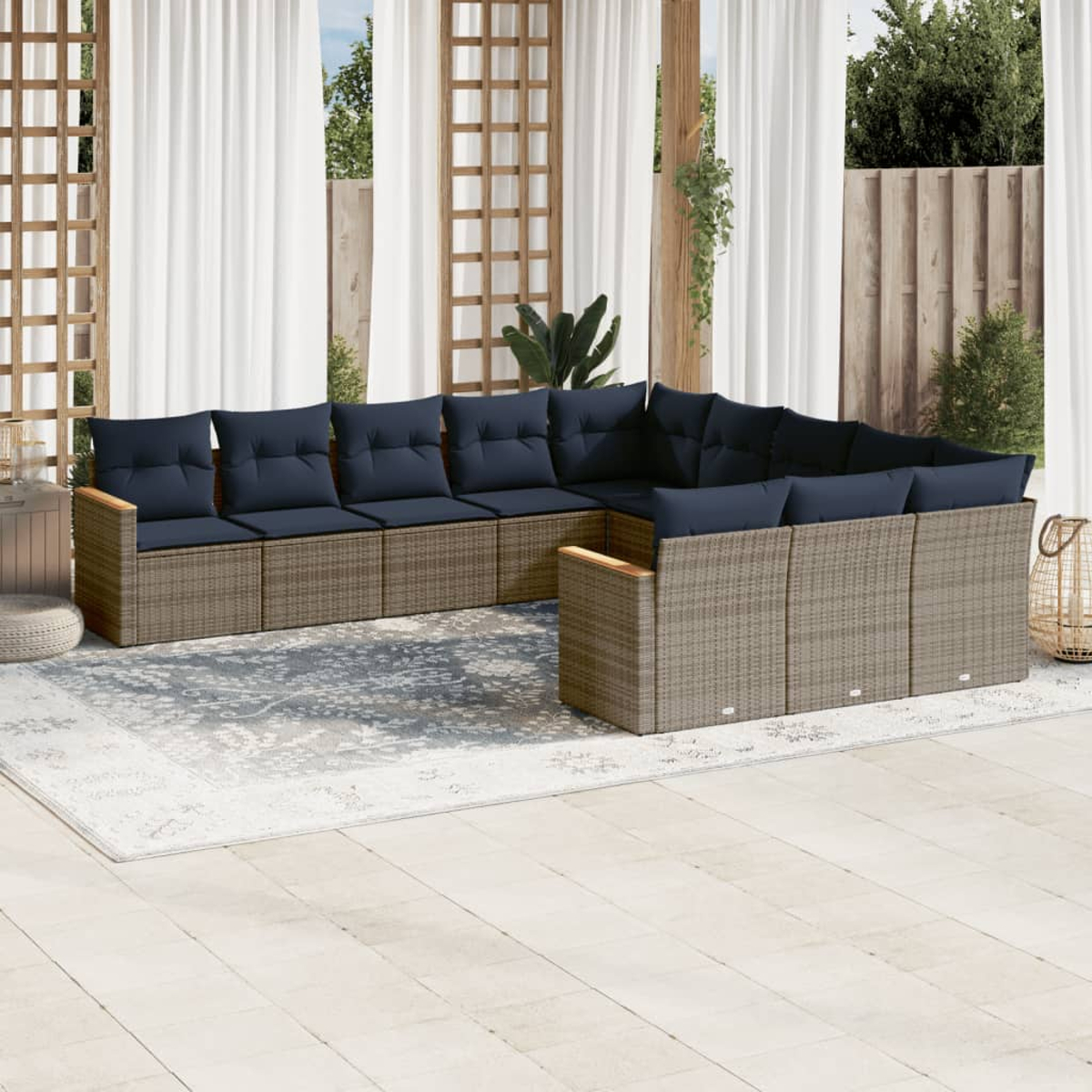 Ein Ecksofa im Freien mit marineblauen Kissen steht auf einem Teppich. Weiße Vorhänge und Holzkonstruktionen befinden sich im Hintergrund.