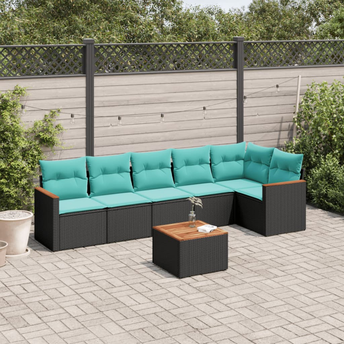 Gartenmöbel: schwarzes Korbgeflecht-Sofa mit türkisfarbenen Kissen, Holzarmlehnen und einem Couchtisch. Im Hintergrund ein Zaun und Grün.