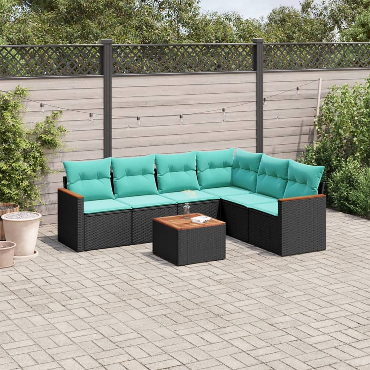 Terrassenset mit schwarzem Korbmöbeln und türkisfarbenen Kissen. Enthält einen Couchtisch. Vor einem Holzzaun und Grün.