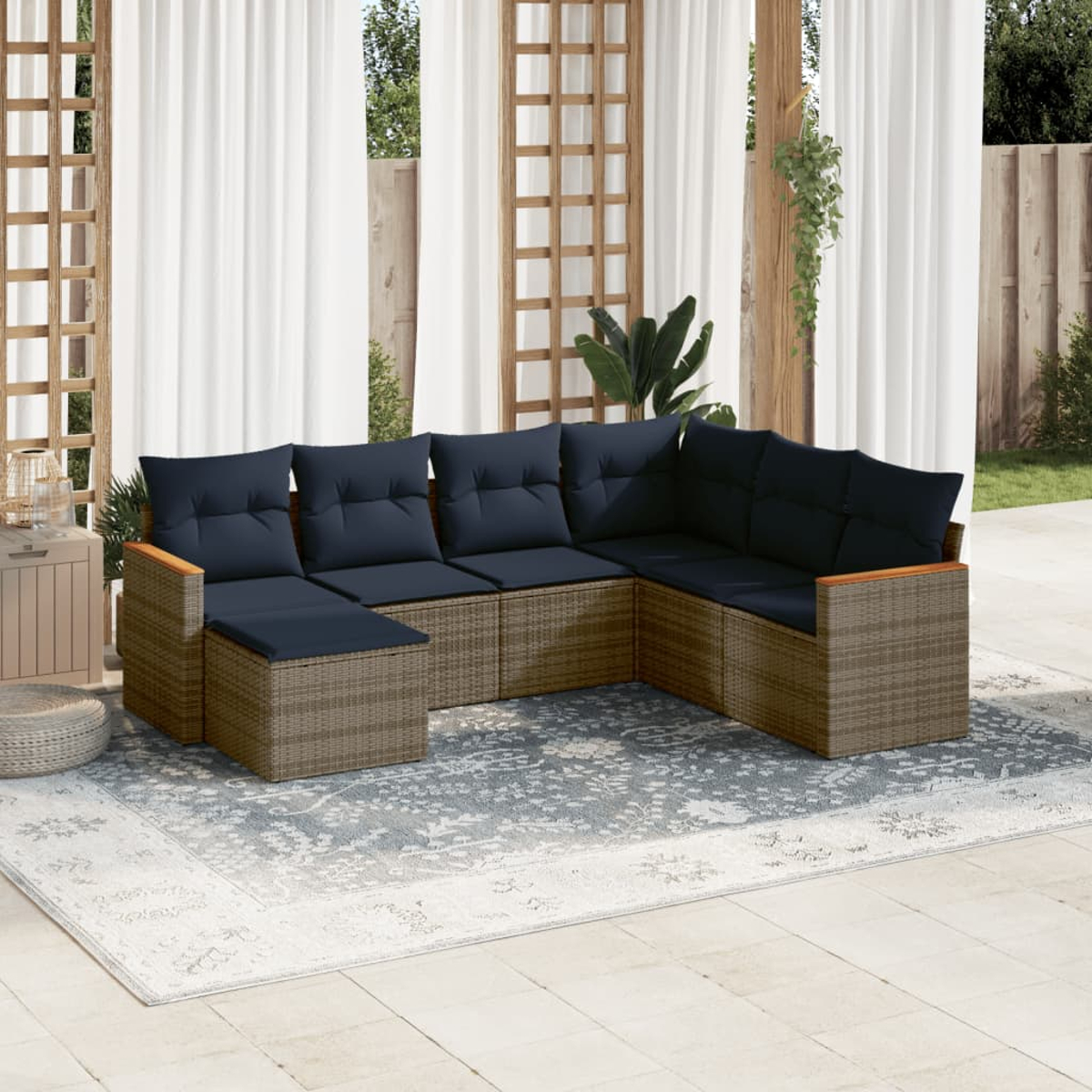 Outdoor-Ecksofa mit marineblauen Kissen auf einem gemusterten Teppich, in der Nähe von Vorhängen und einem Holzgitter. Hintergrund mit Grün und Holzzaun.