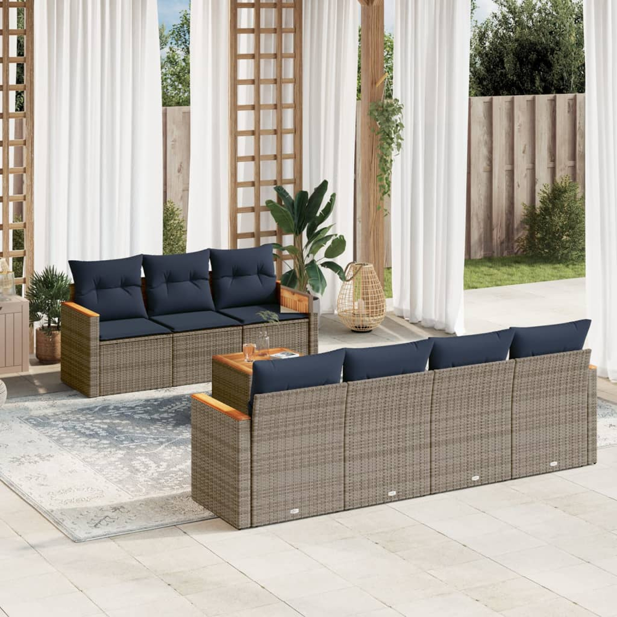 Garten-Sitzgruppe. Zwei Korbs Sofas mit marineblauen Kissen, ein kleiner Tisch und weiße Vorhänge im Hintergrund. Unter den Möbeln liegt ein Teppich.