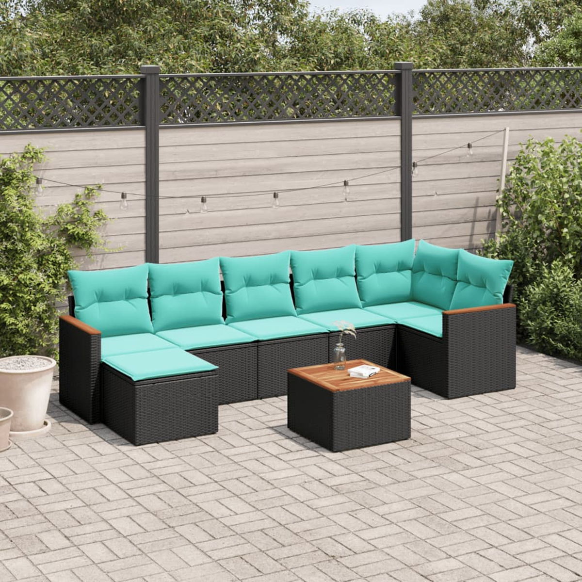 Outdoor-Ecksofa mit tealfarbenen Kissen und schwarzem Korbgewebe. Davor steht ein kleiner Holztisch. Im Hintergrund ein Zaun und Pflanzen.