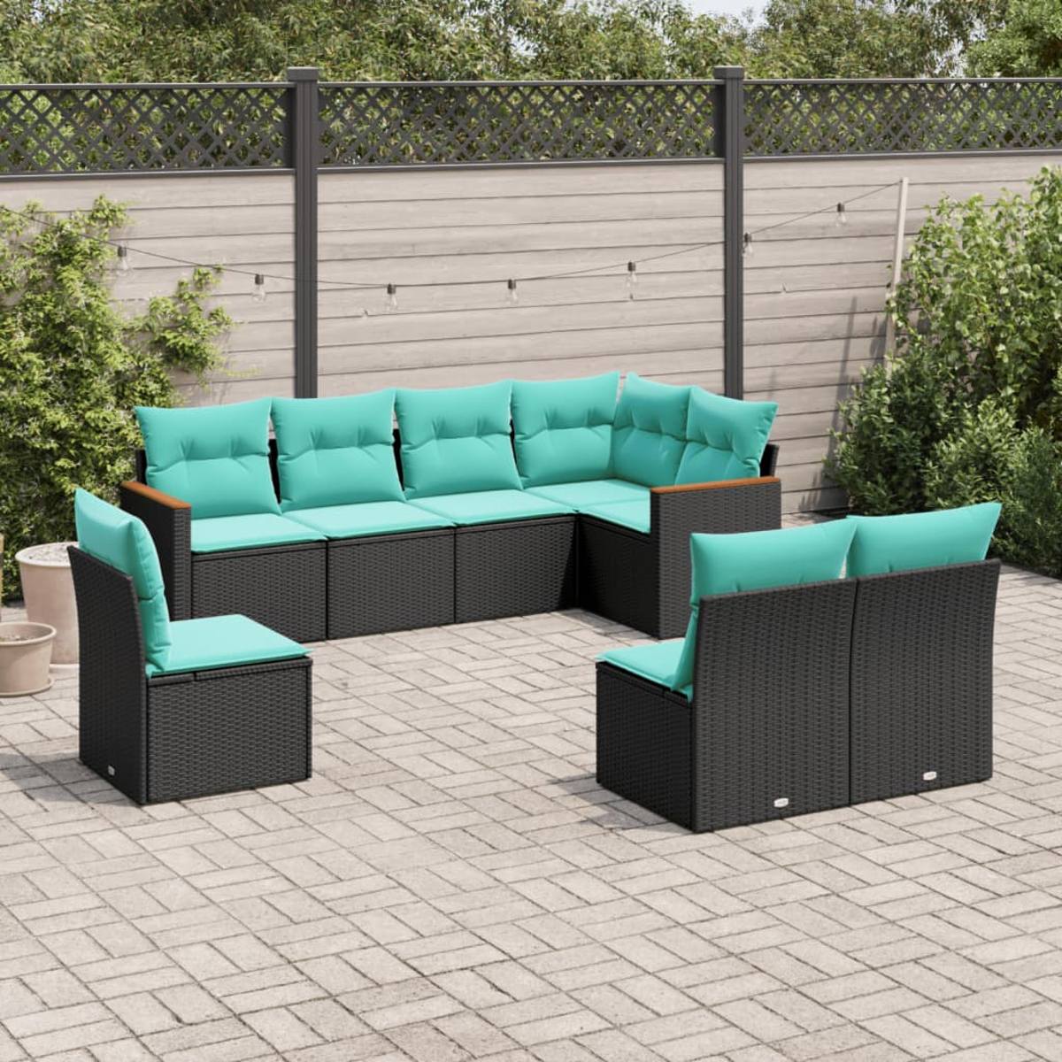 Gartenmöbel-Set: schwarze Korbsessel mit türkisfarbenen Kissen auf einer Ziegelterrasse. Ein Holzzaun und Grünzeug sind im Hintergrund.