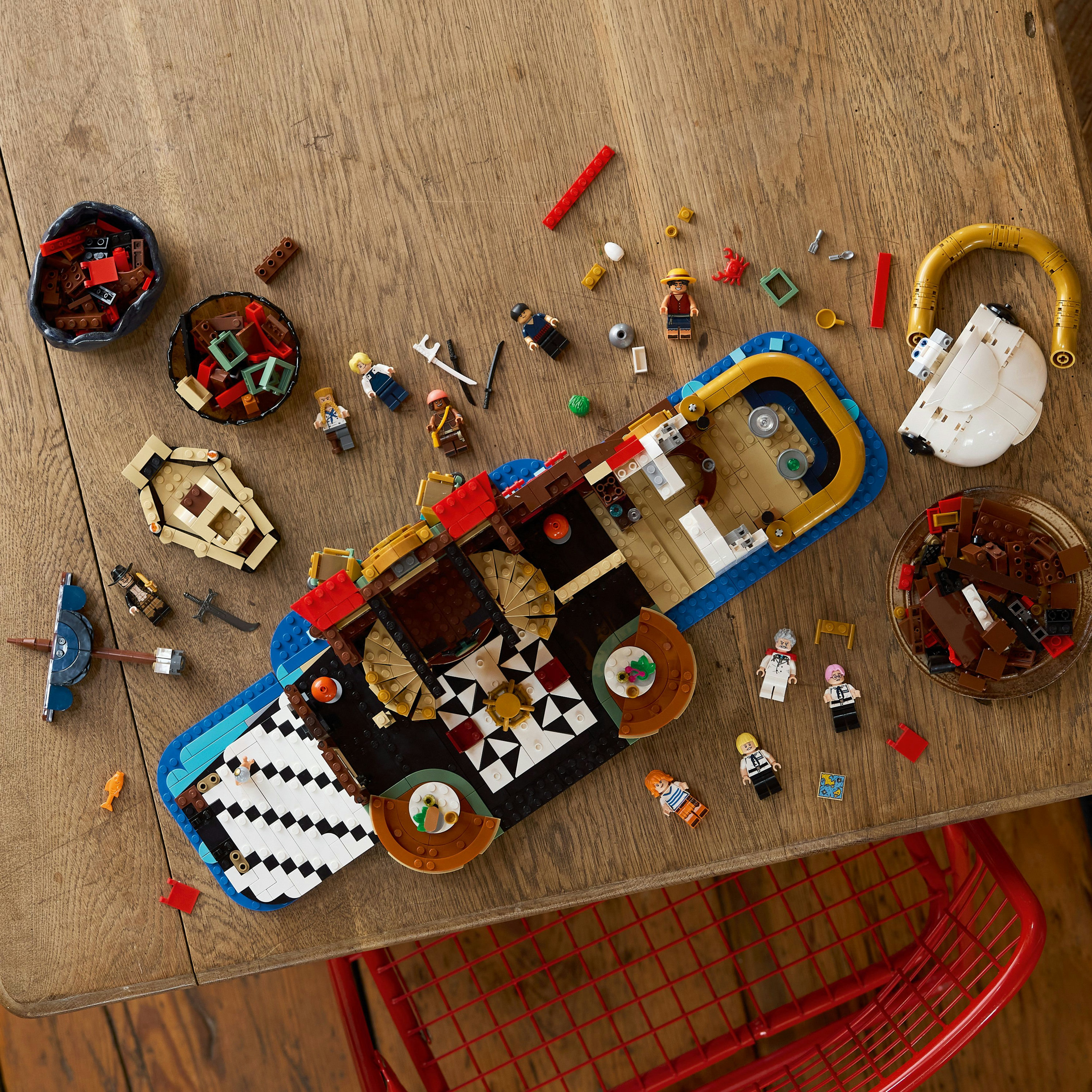 Statek piracki Lego na drewnianym stole. Mini figurki i różne elementy rozrzucone wokół statku, z miskami klocków.