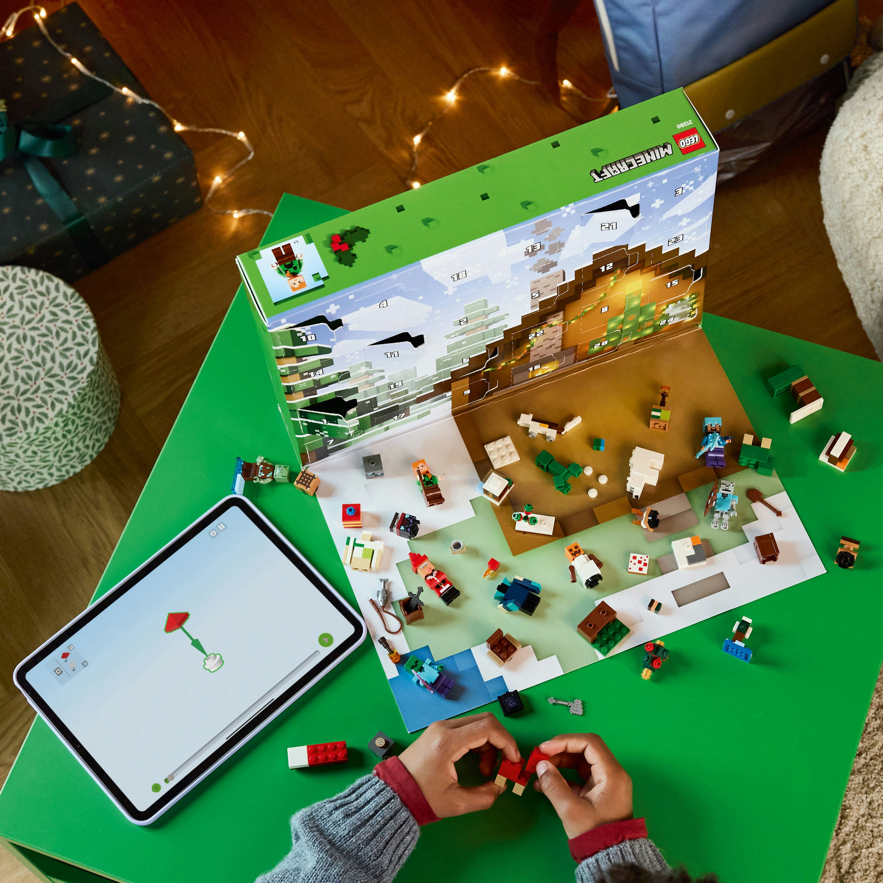 Kalendarz adwentowy Minecraft z klockami Lego na zielonym stole, dłonie dziecka składające Lego, tablet.