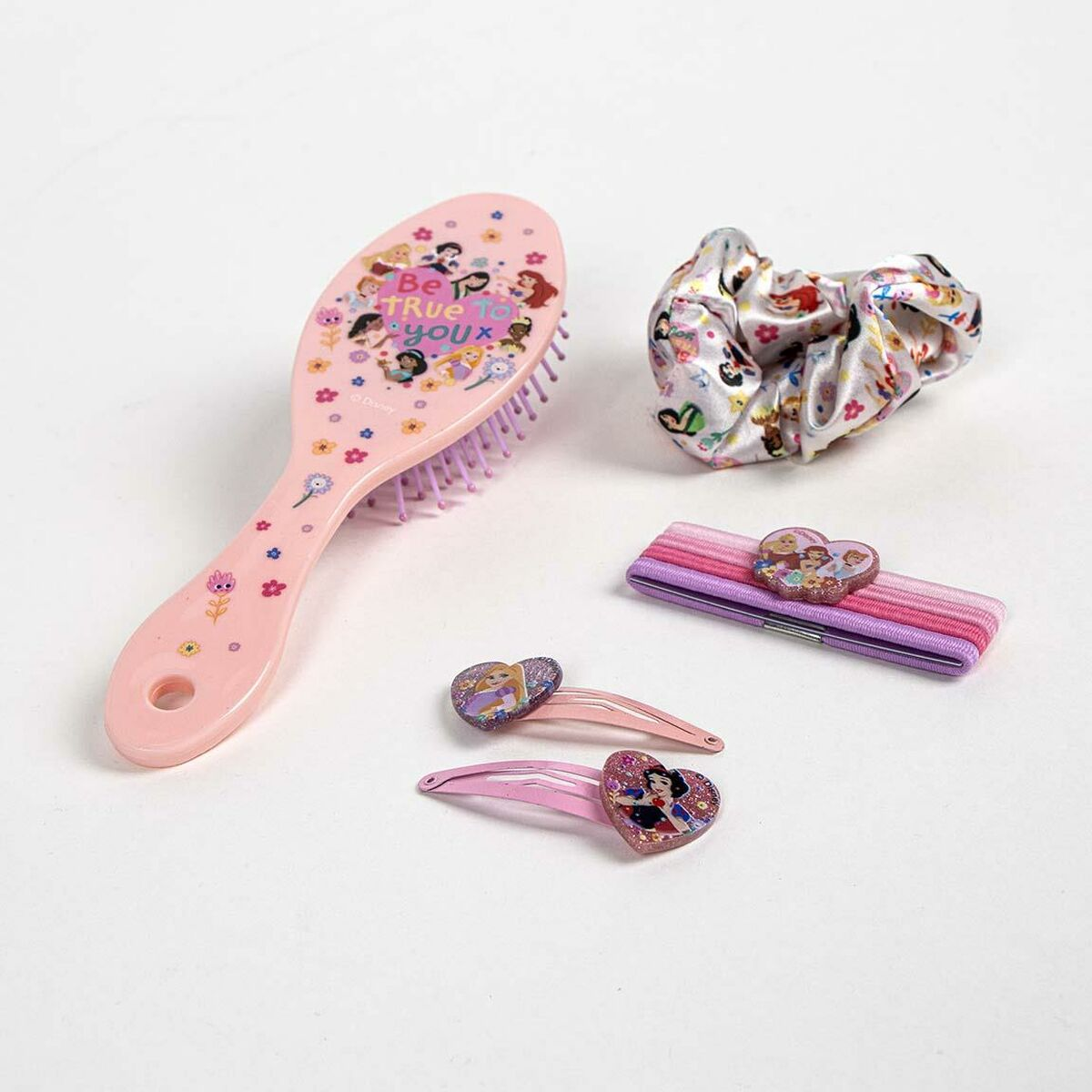 Eine rosa Haarbürste, ein Scrunchie, Haargummis und -clips mit Disney-Prinzessinnen-Motiven auf weißem Grund.