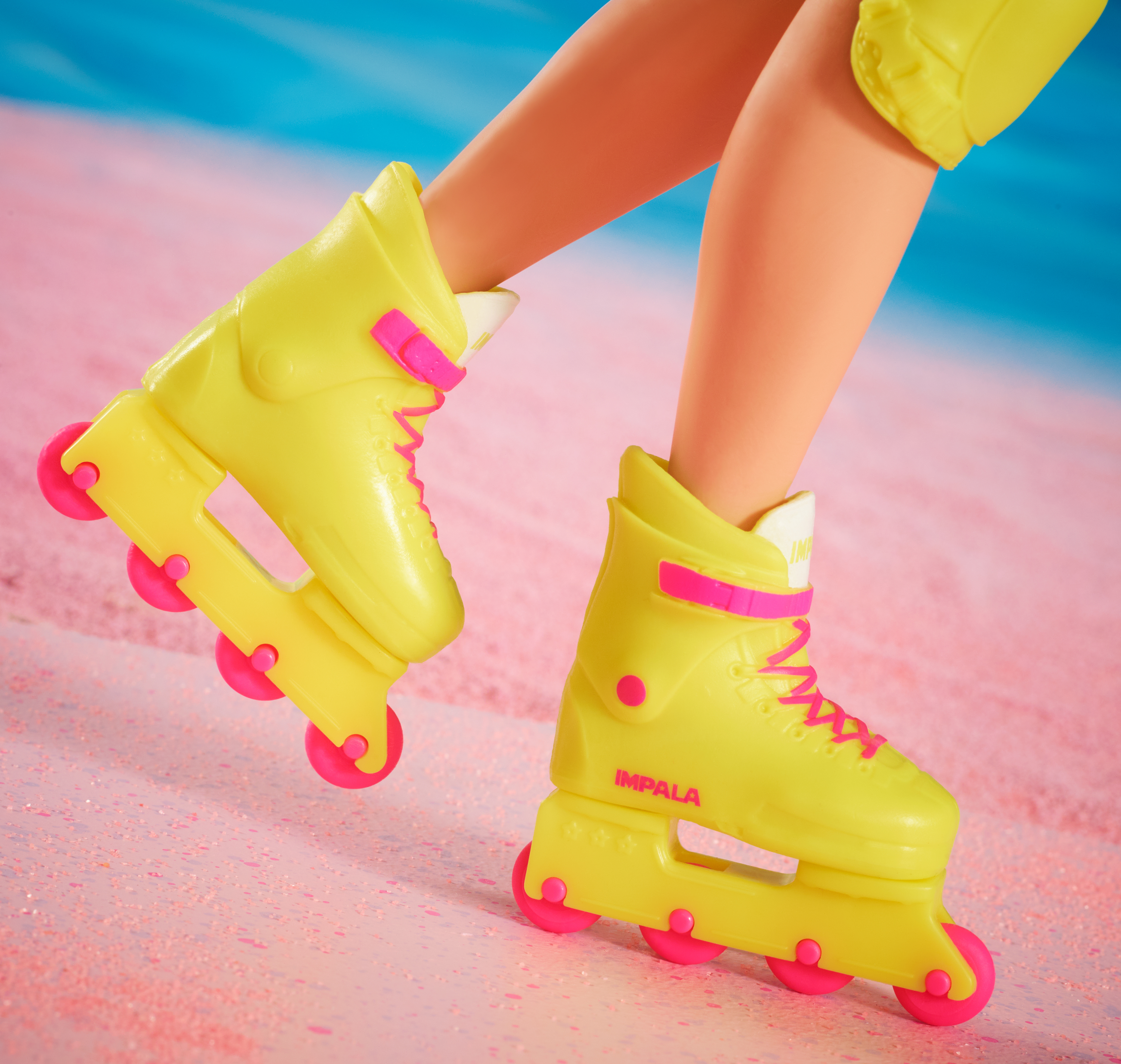 Primer plano de piernas de muñeca con patines amarillos con ruedas y cordones rosas. El fondo es rosa y azul.