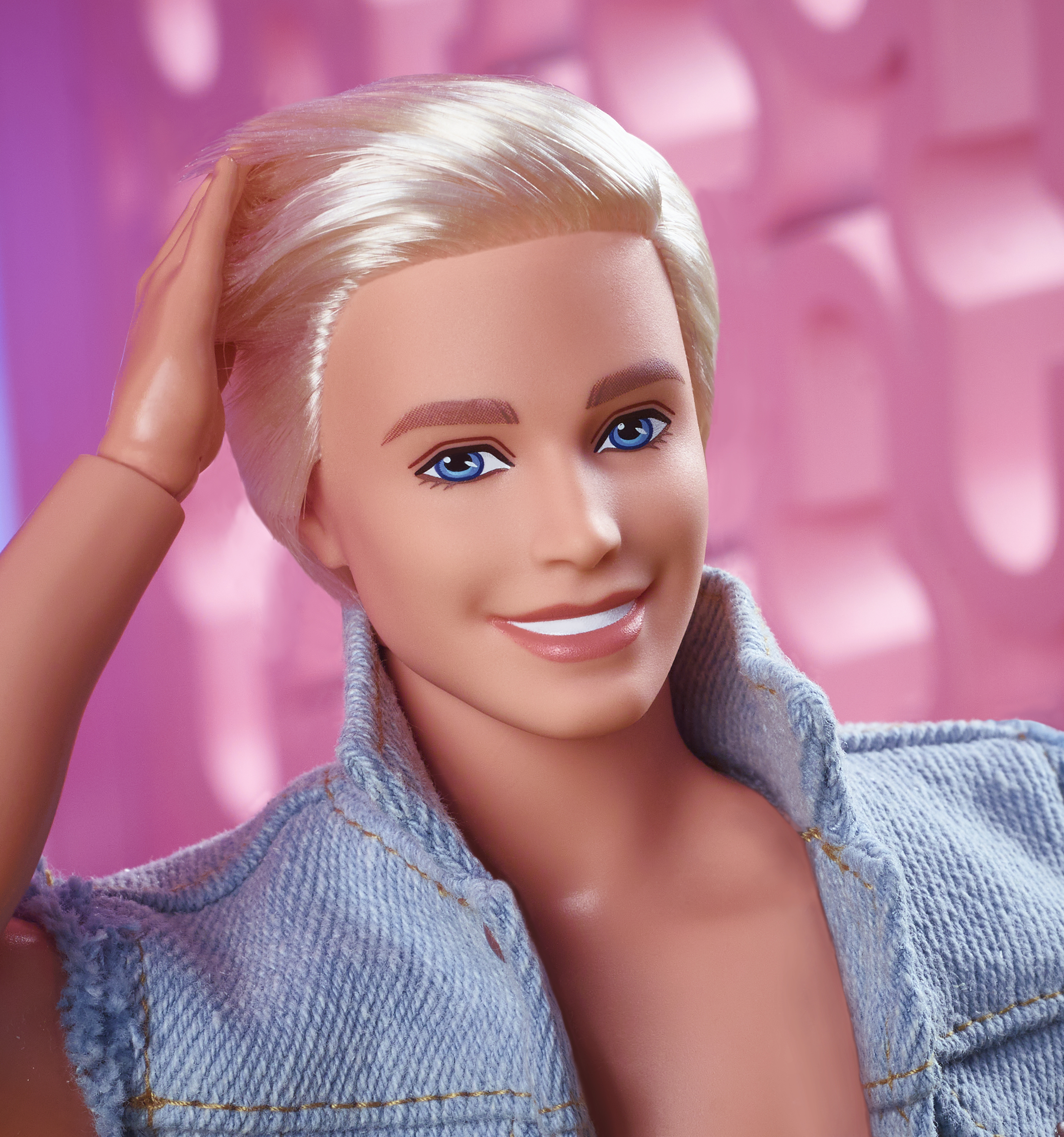 Un muñeco Ken con pelo rubio, ojos azules y una chaqueta vaquera. Sonríe con la mano en la cabeza.