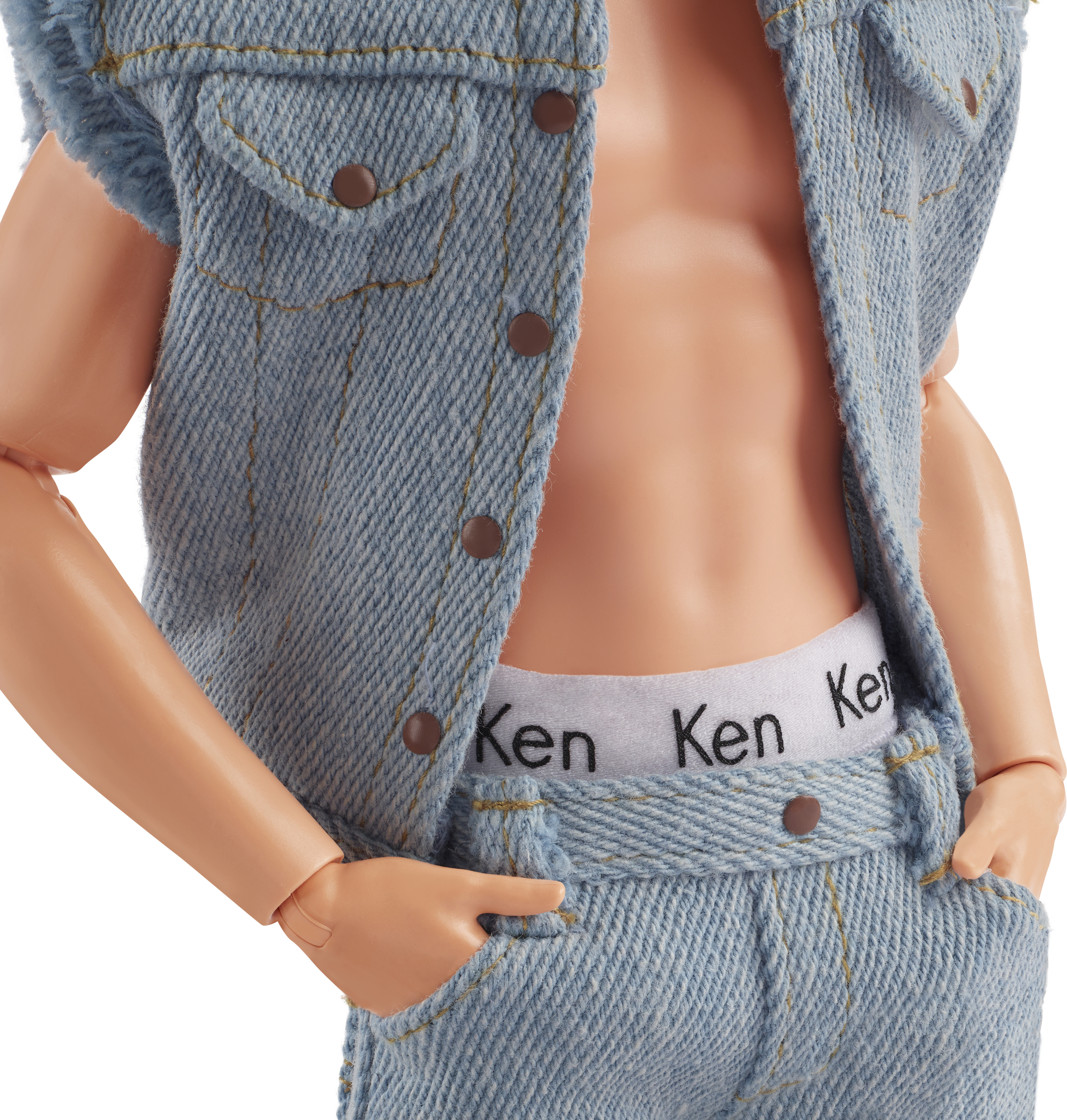 Muñeco Ken con chaleco y vaqueros de mezclilla, mostrando una cintura blanca con "Ken" impreso. Manos en bolsillos.