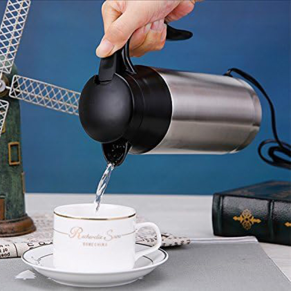 Eine Hand gießt Wasser aus einem silbernen und schwarzen Wasserkocher in eine weiße Teetasse auf einer Untertasse. Eine Windmühle und ein Buch sind im Hintergrund.