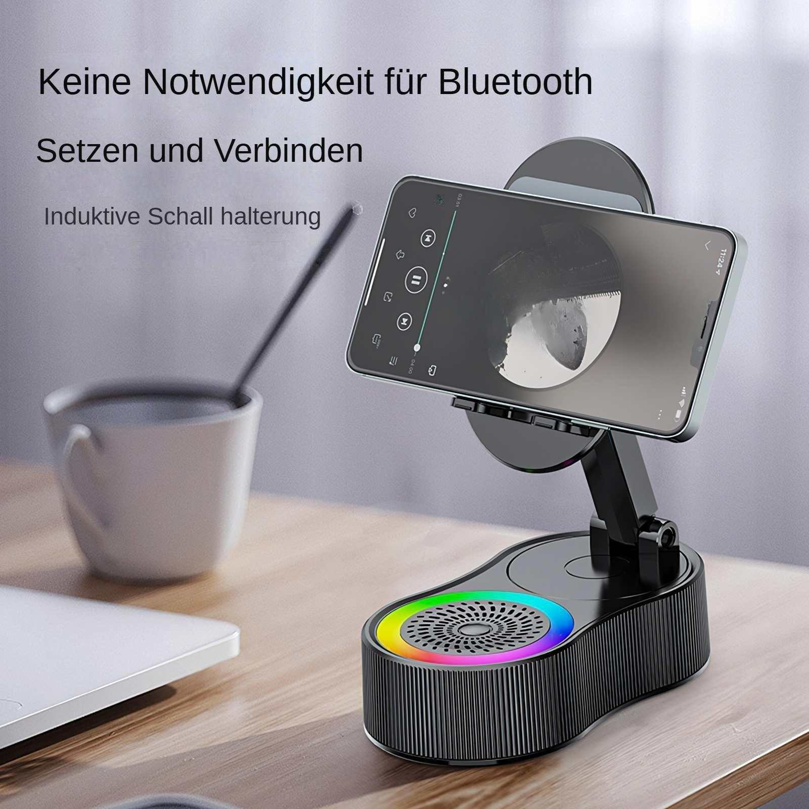 Ein Telefon ist auf einem schwarzen Gerät mit einem regenbogenfarbenen Lautsprecher angedockt. Eine weiße Tasse und ein Laptop sind im Hintergrund.