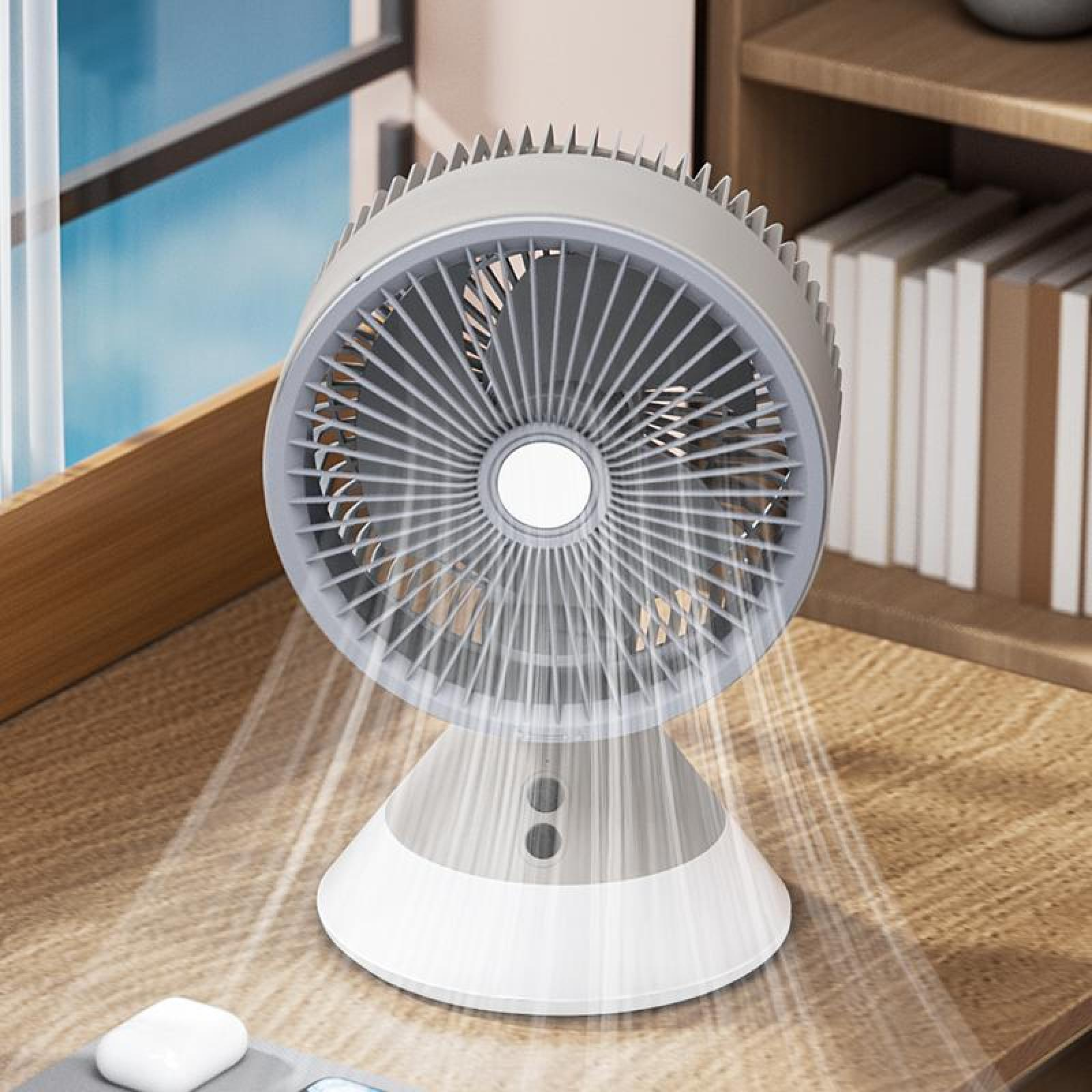 Ein weiß-grauer Tischventilator steht auf einem Holztisch. Luft wird ausgeblasen. Bücher und Fenster im Hintergrund.