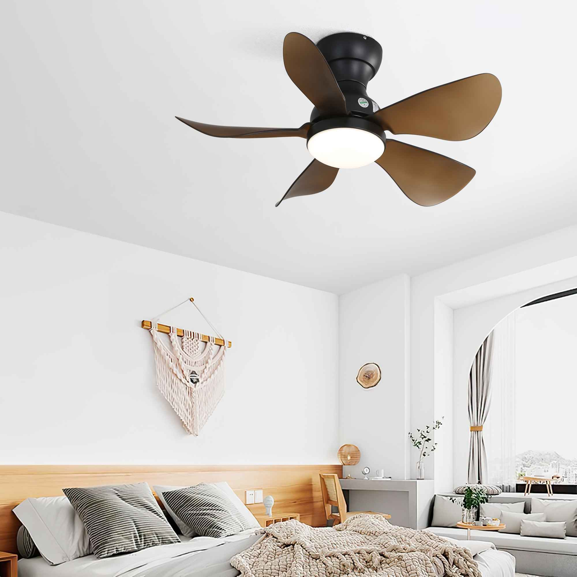 Ein Schlafzimmer mit Deckenventilator, Bett und Sofa. Der Ventilator hat braune Flügel. Das Bett hat Kissen und eine Decke. Ein Fenster ist sichtbar.