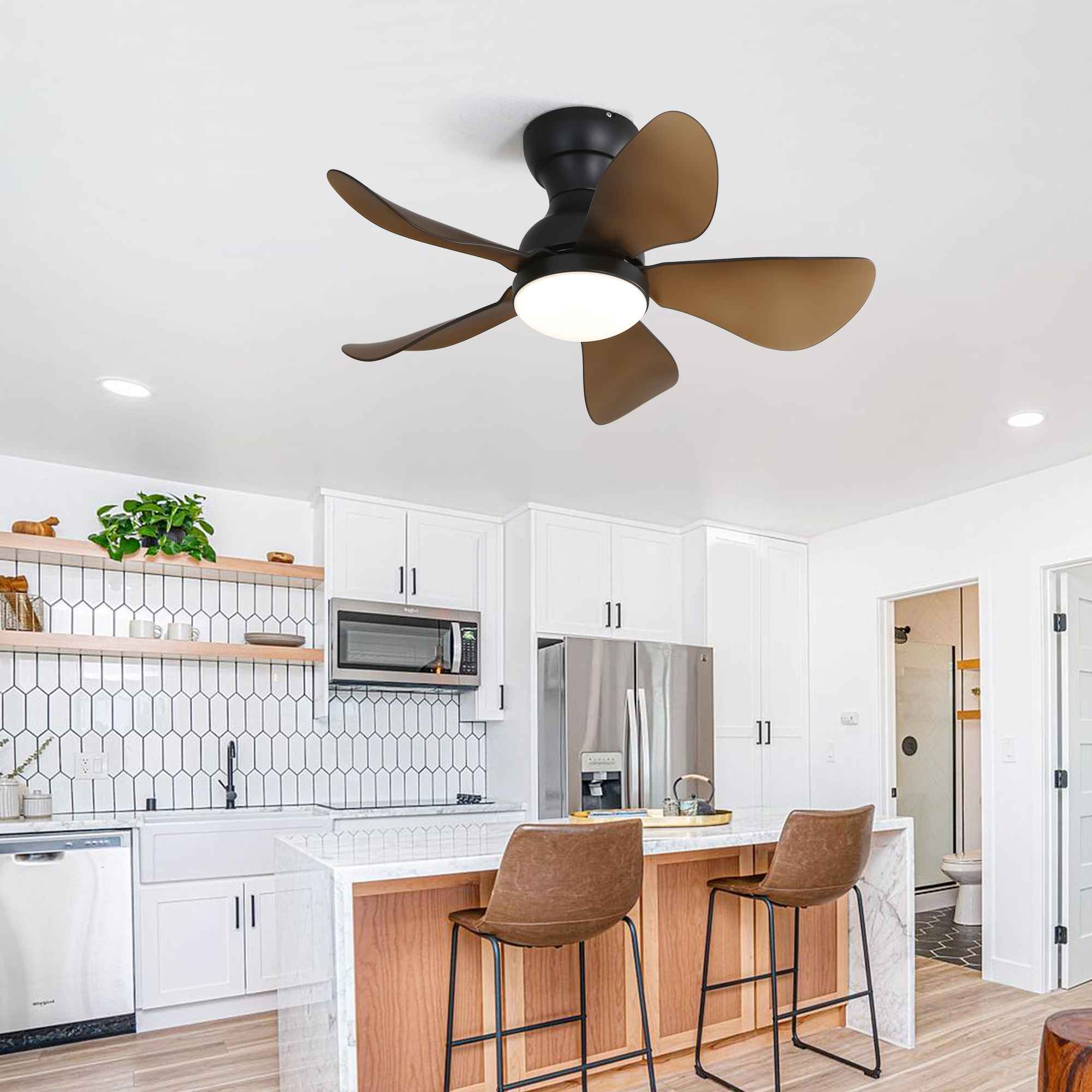 Eine Küchenszene mit Deckenventilator. Weiße Schränke, eine Insel mit Hockern und ein Kühlschrank aus Edelstahl sind sichtbar.