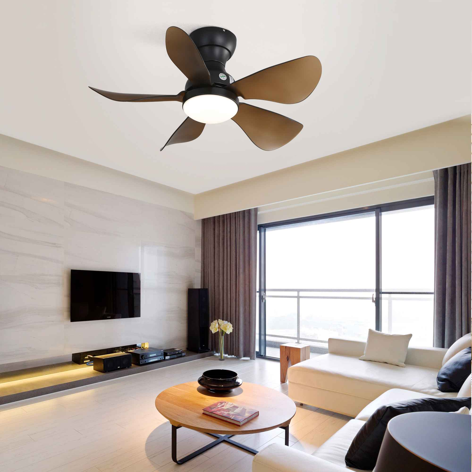 Ein modernes Wohnzimmer mit Deckenventilator, großem Fernseher, weißem Sofa, rundem Holztisch und großem Fenster.