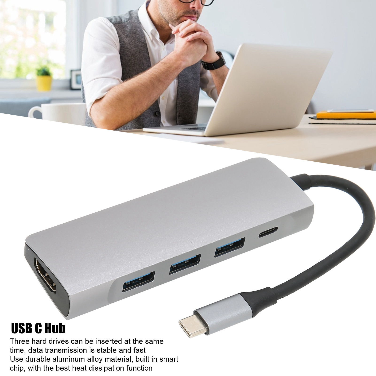 Ein Mann benutzt einen Laptop, ein USB-C-Hub ist im Vordergrund zu sehen. Der Hub ist silberfarben und hat mehrere Anschlüsse.