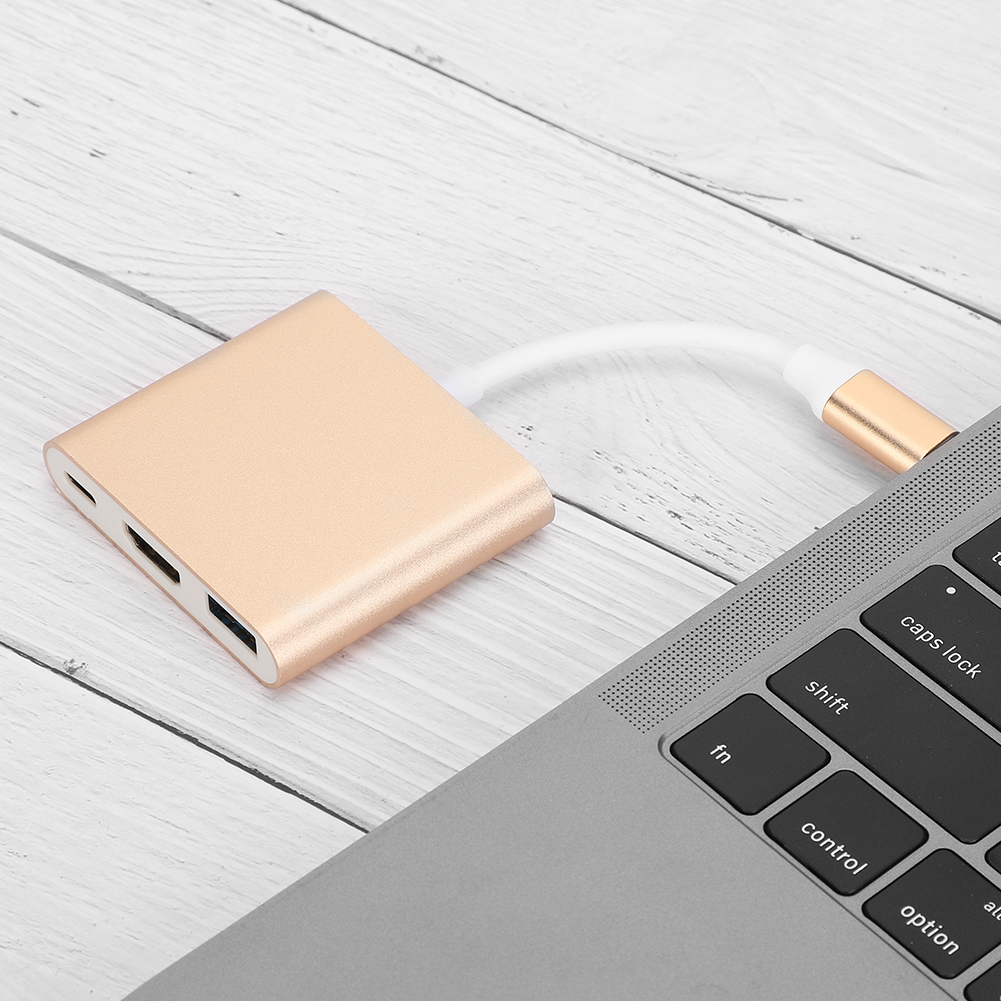 Ein goldener Adapter, der über ein weißes Kabel mit einem Laptop verbunden ist. Der Adapter befindet sich auf einer weißen Holzoberfläche.