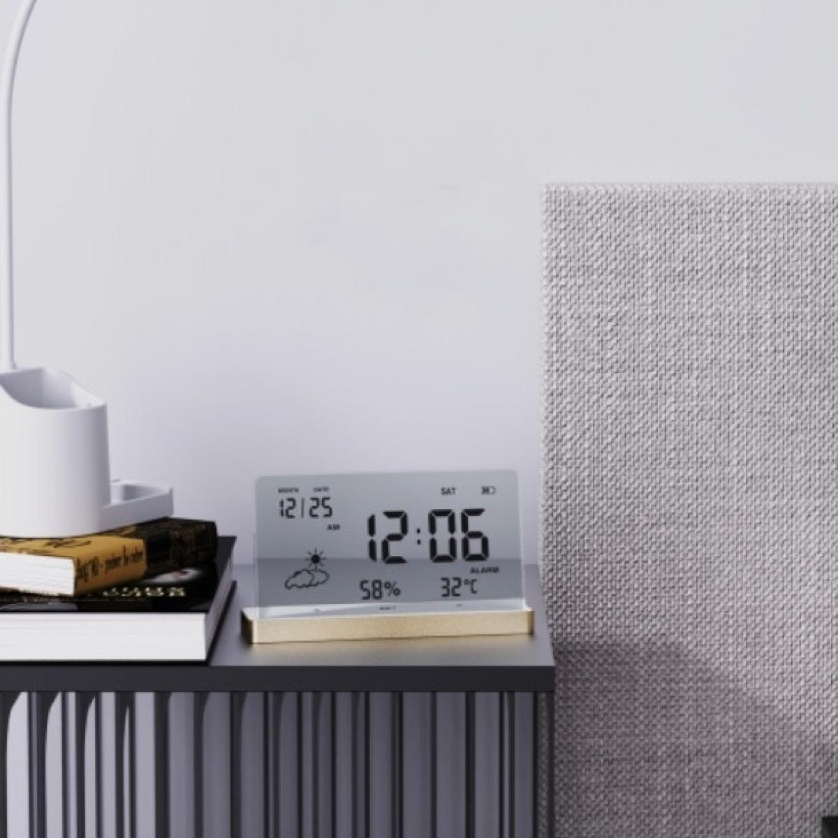 Eine Digitaluhr zeigt 12:06 mit Wetterinformationen an. Sie steht auf einem schwarzen Tisch mit Büchern und einer Lampe. Im Hintergrund ist eine strukturierte graue Wand.