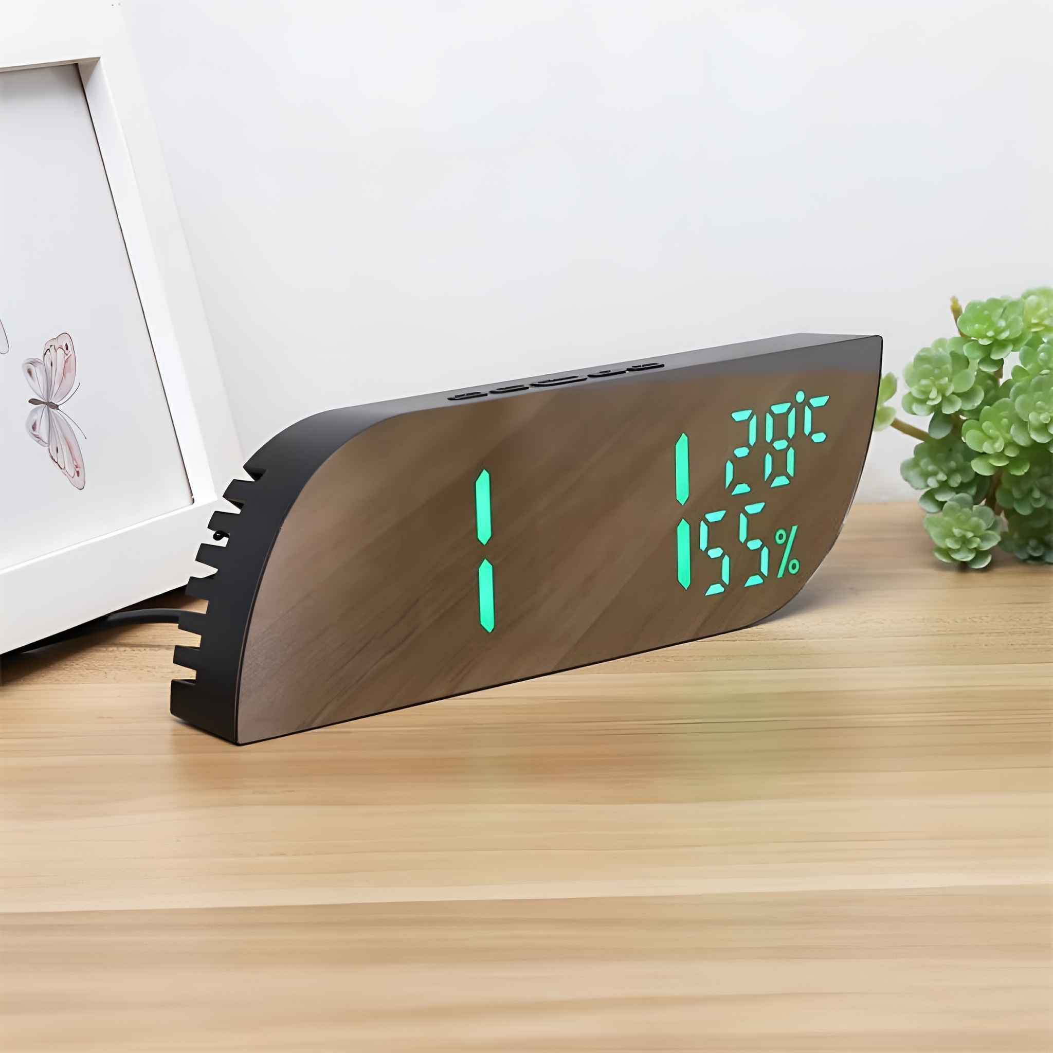 Eine Digitaluhr zeigt Zeit und Luftfeuchtigkeit an. Ein weißer Bilderrahmen und eine grüne Pflanze befinden sich im Hintergrund.