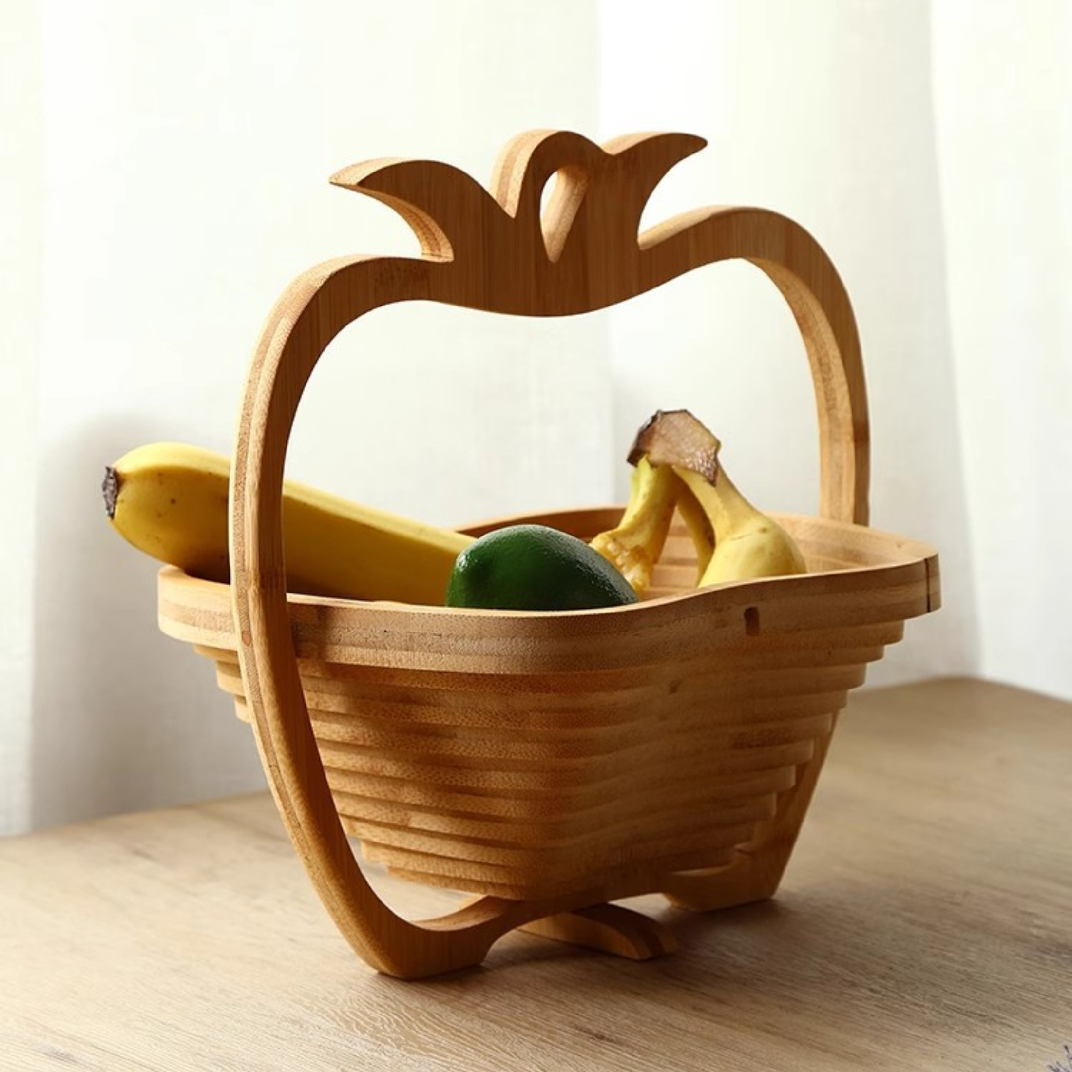 Ein holzförmiger Apfelkorb mit Bananen und Avocado. Der Korb steht auf einem Holztisch, mit weißem Hintergrund.