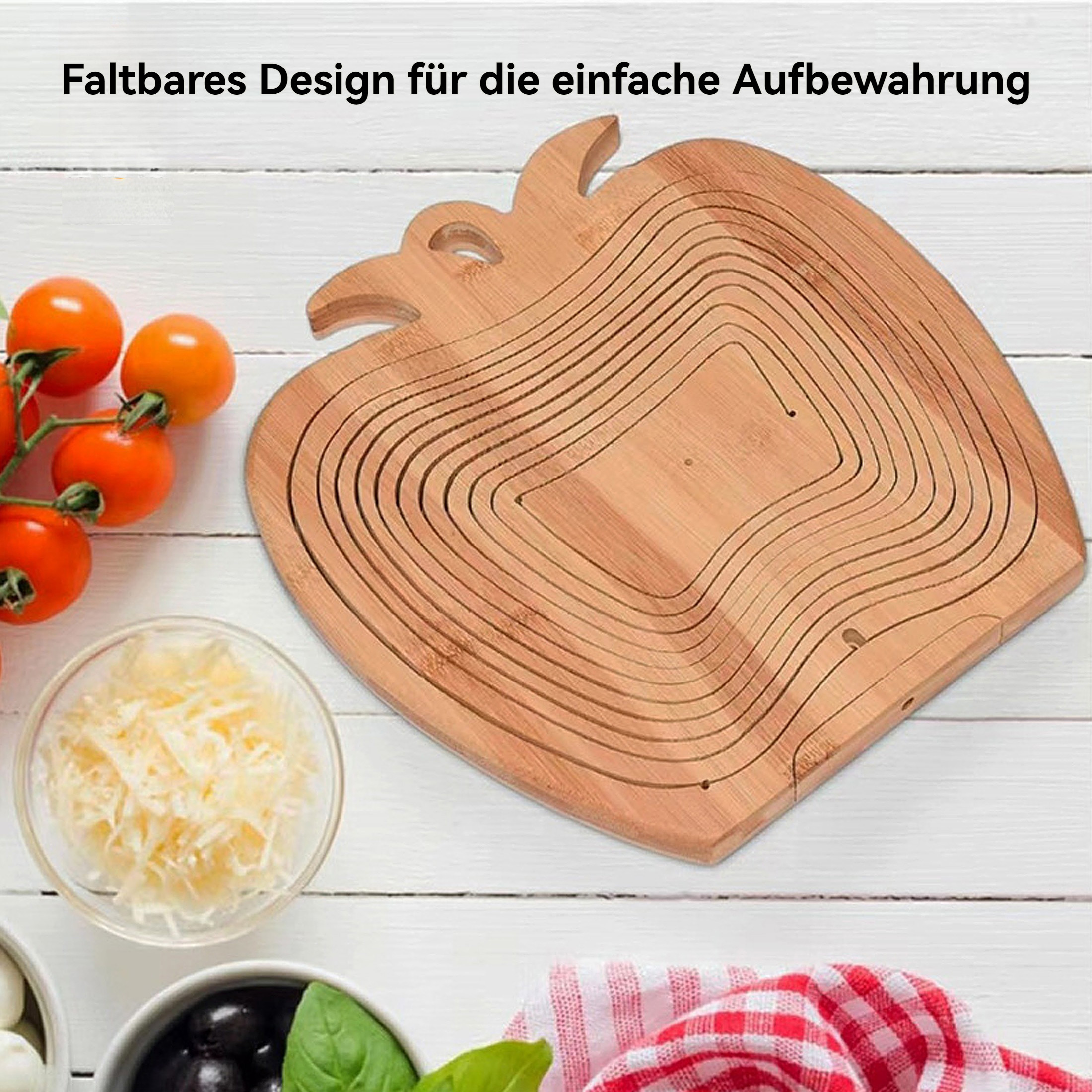 Ein holzfarbener Obstkorb in Apfelform mit Tomaten, Käse, Oliven und einem rot-weiß karierten Tuch auf einem weißen Holztisch.