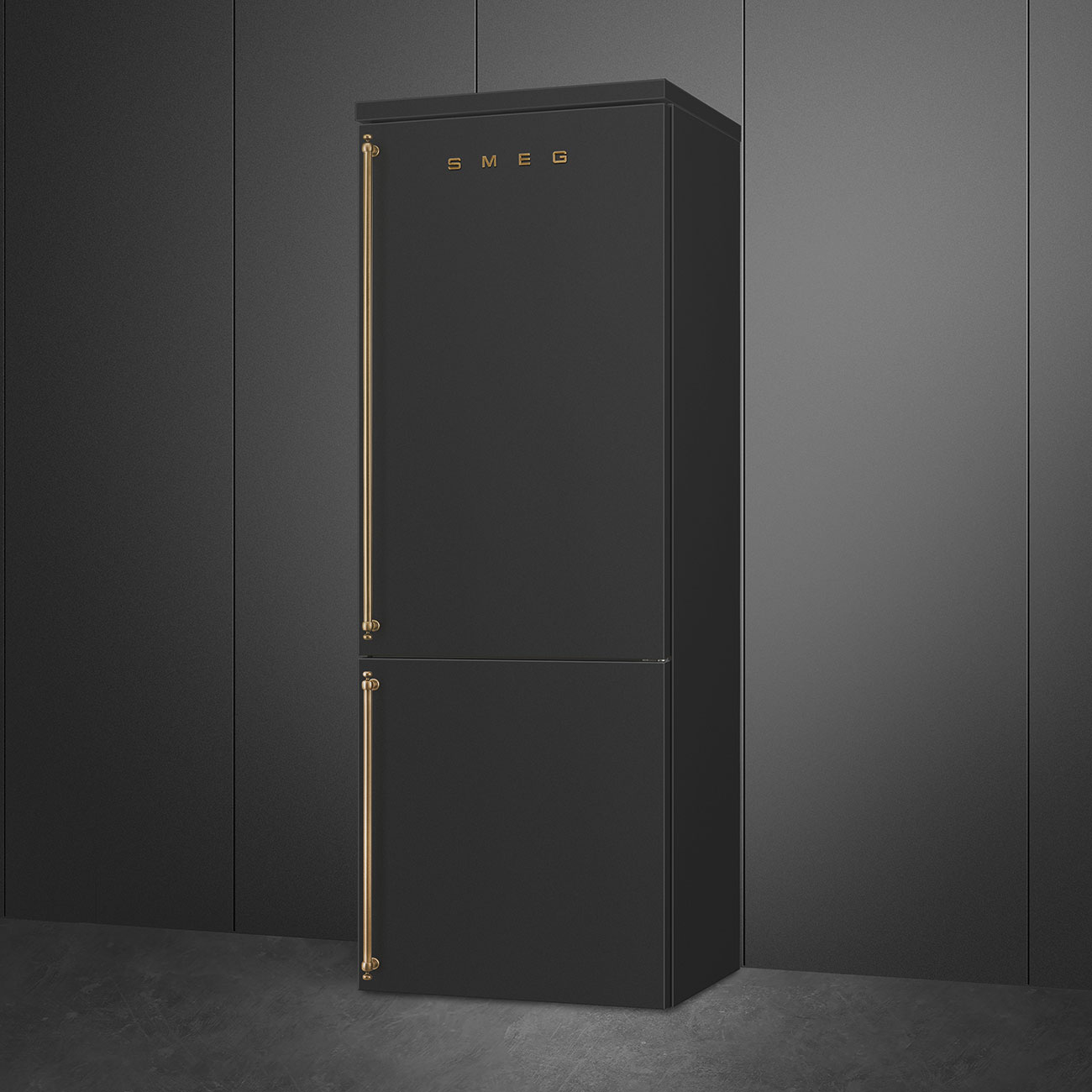 Un refrigerador SMEG negro con manijas doradas se encuentra contra una pared gris oscuro. El refrigerador tiene dos puertas.