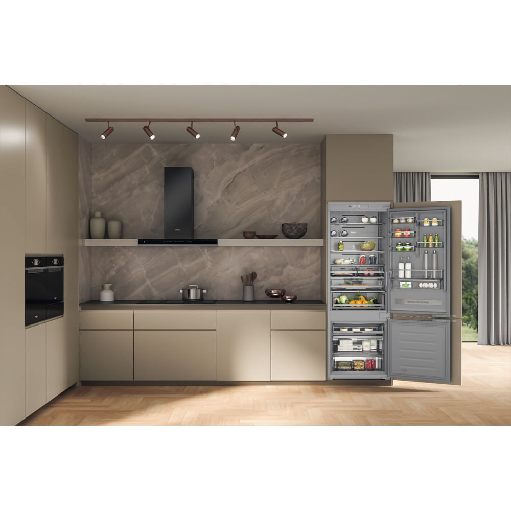 Una cucina moderna con frigorifero aperto. Armadi beige, pavimento in legno e cappa scura. Il frigorifero è pieno di cibo.