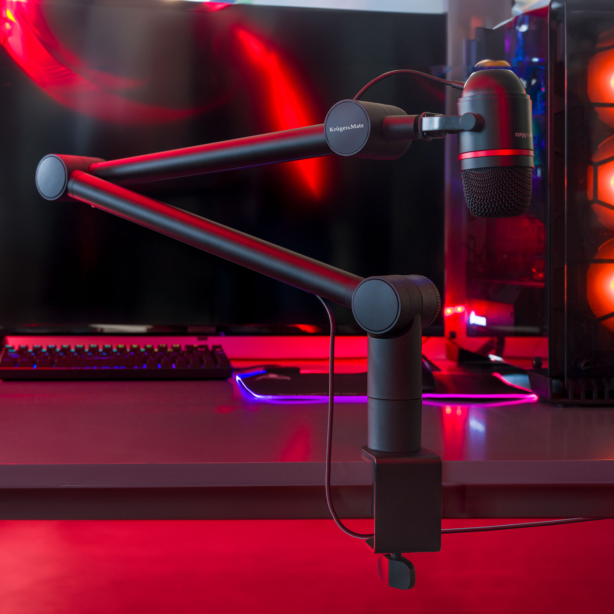 Czarny mikrofon na statywie, biurku i komputerze. Czerwone oświetlenie. Ramię mikrofonu jest regulowane. Widoczna klawiatura.