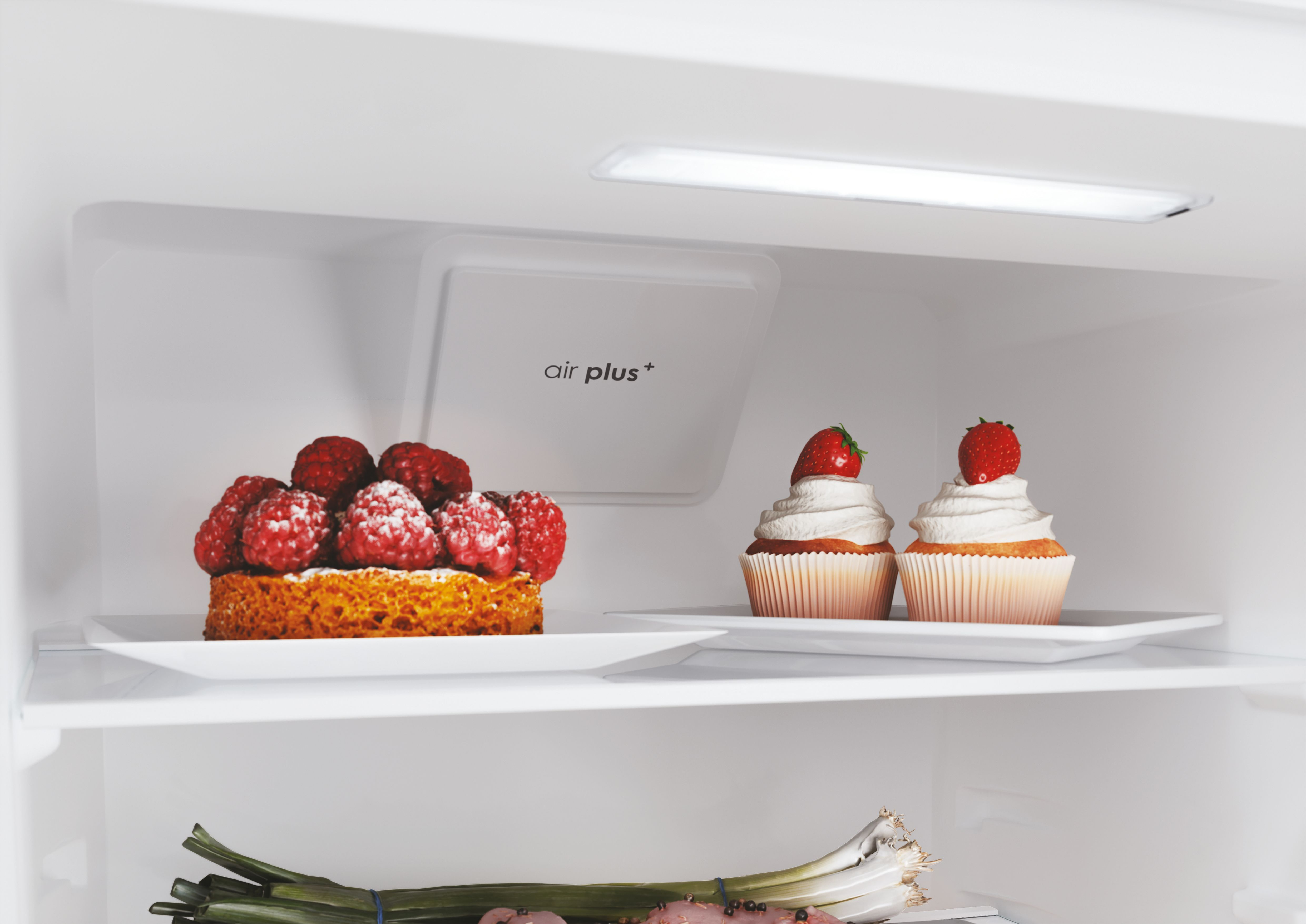 All'interno di un frigorifero: torta di lamponi, cupcake con fragole, cipollotti e interno bianco.