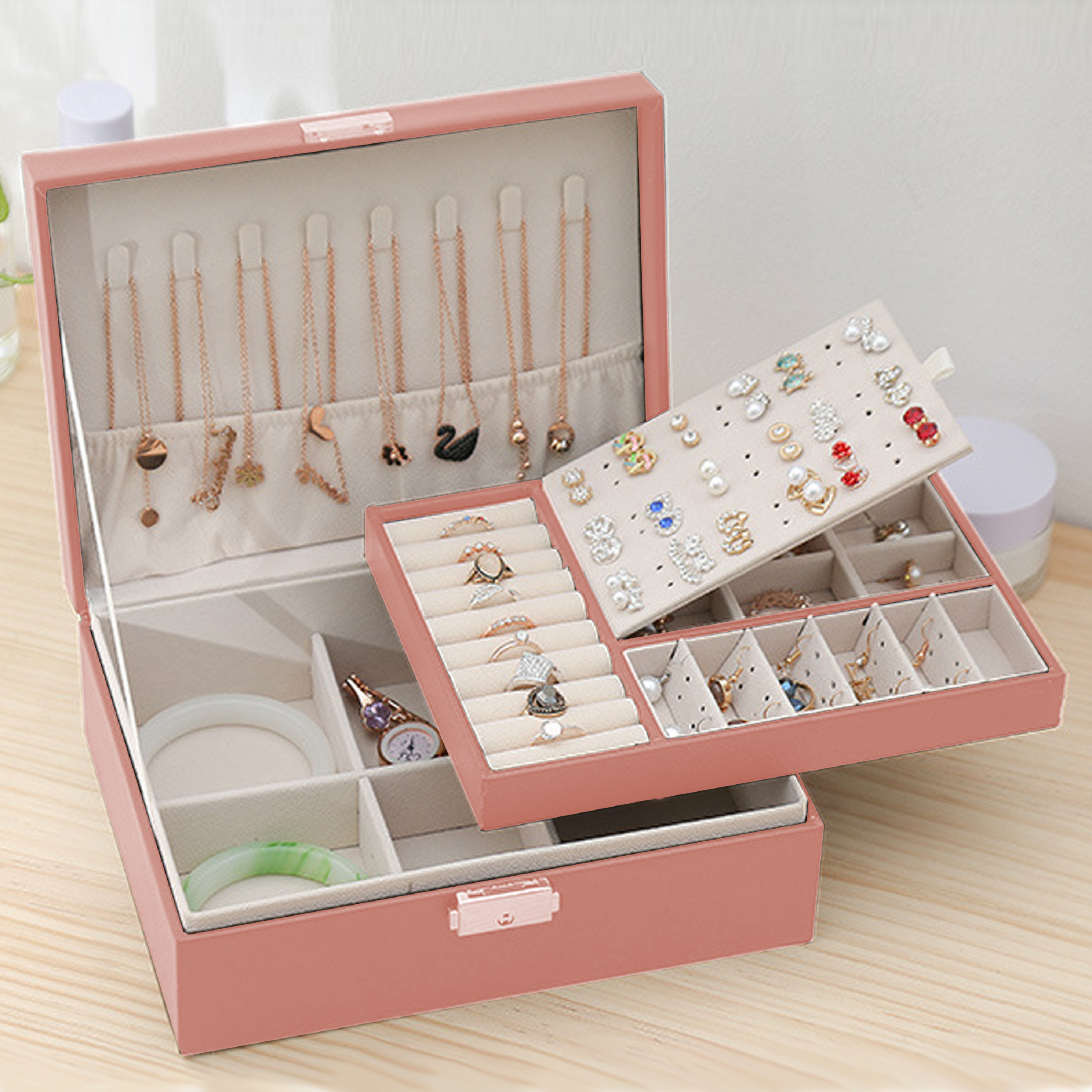 Geöffnete rosa Schmuckschatulle, die Halsketten, Ringe, Ohrringe und Armbänder zeigt. Die Schachtel steht auf Holz.