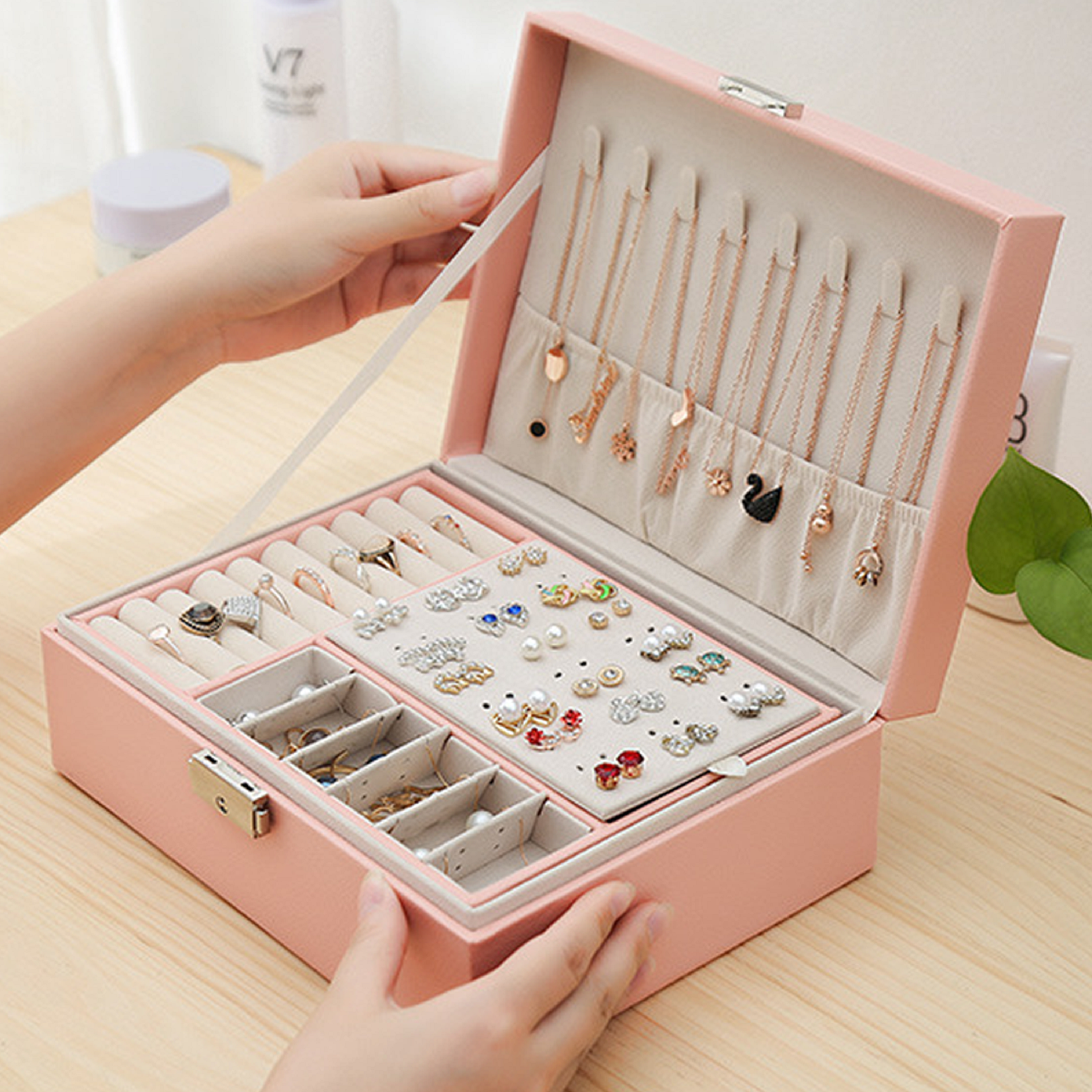 Eine rosa Schmuckschatulle mit Schmuck darin. Eine Hand öffnet den Deckel. Die Box steht auf einem Holztisch.