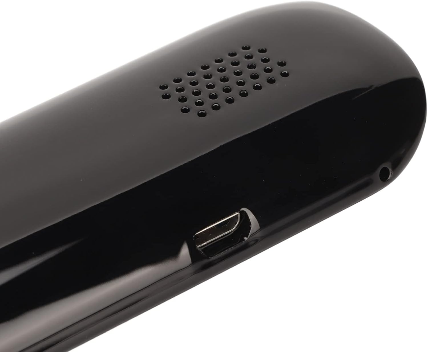 Nahaufnahme eines schwarzen, glänzenden Geräts. Es hat ein Lautsprechergitter, einen USB-Anschluss und ein kleines Loch. Die Oberfläche reflektiert das Licht.