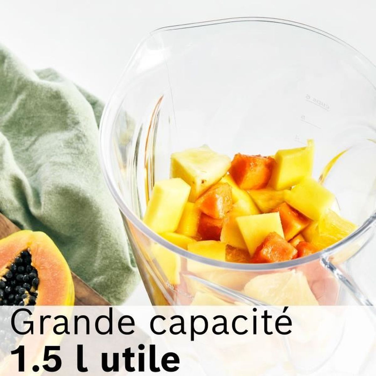 Una ciotola trasparente con mango, ananas e papaya tritati. A sinistra un panno verde e in basso a sinistra una mezza papaya.