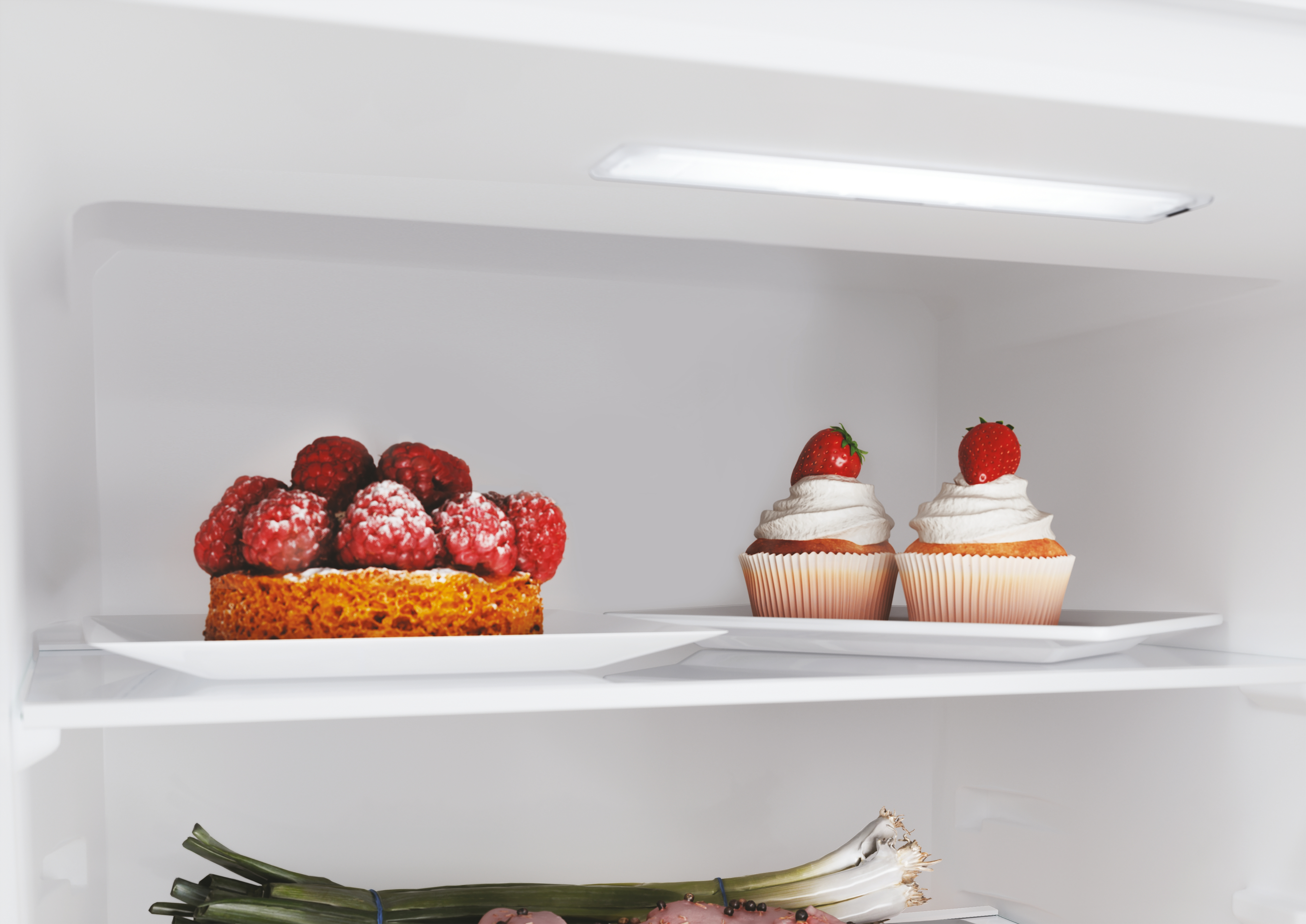 Dentro un frigo, crostata di lamponi e due cupcake con fragole. Cipolline in basso.