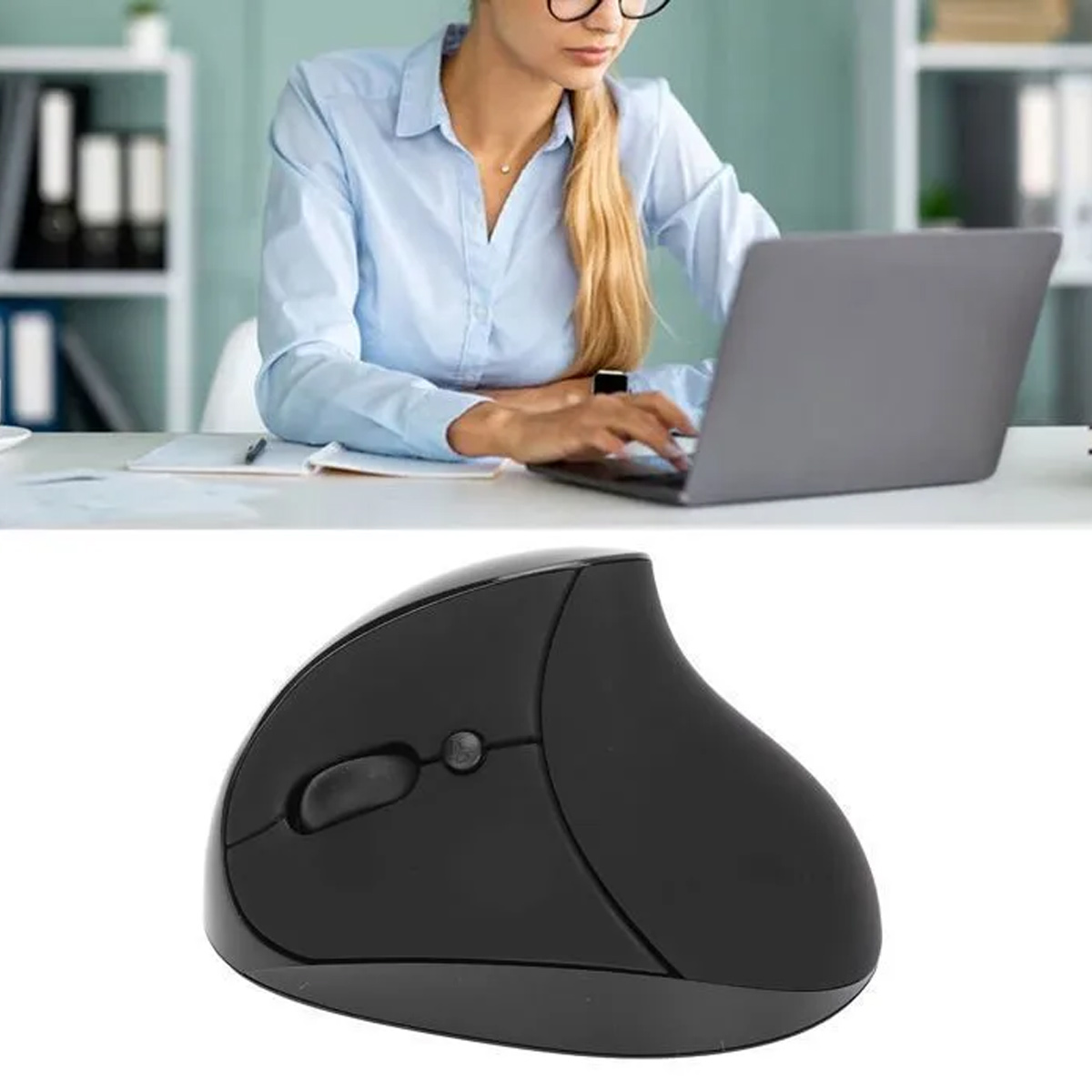 Eine Frau mit Brille tippt auf einem Laptop. Im Vordergrund befindet sich eine schwarze ergonomische Maus. Büroumgebung mit Regalen im Hintergrund.