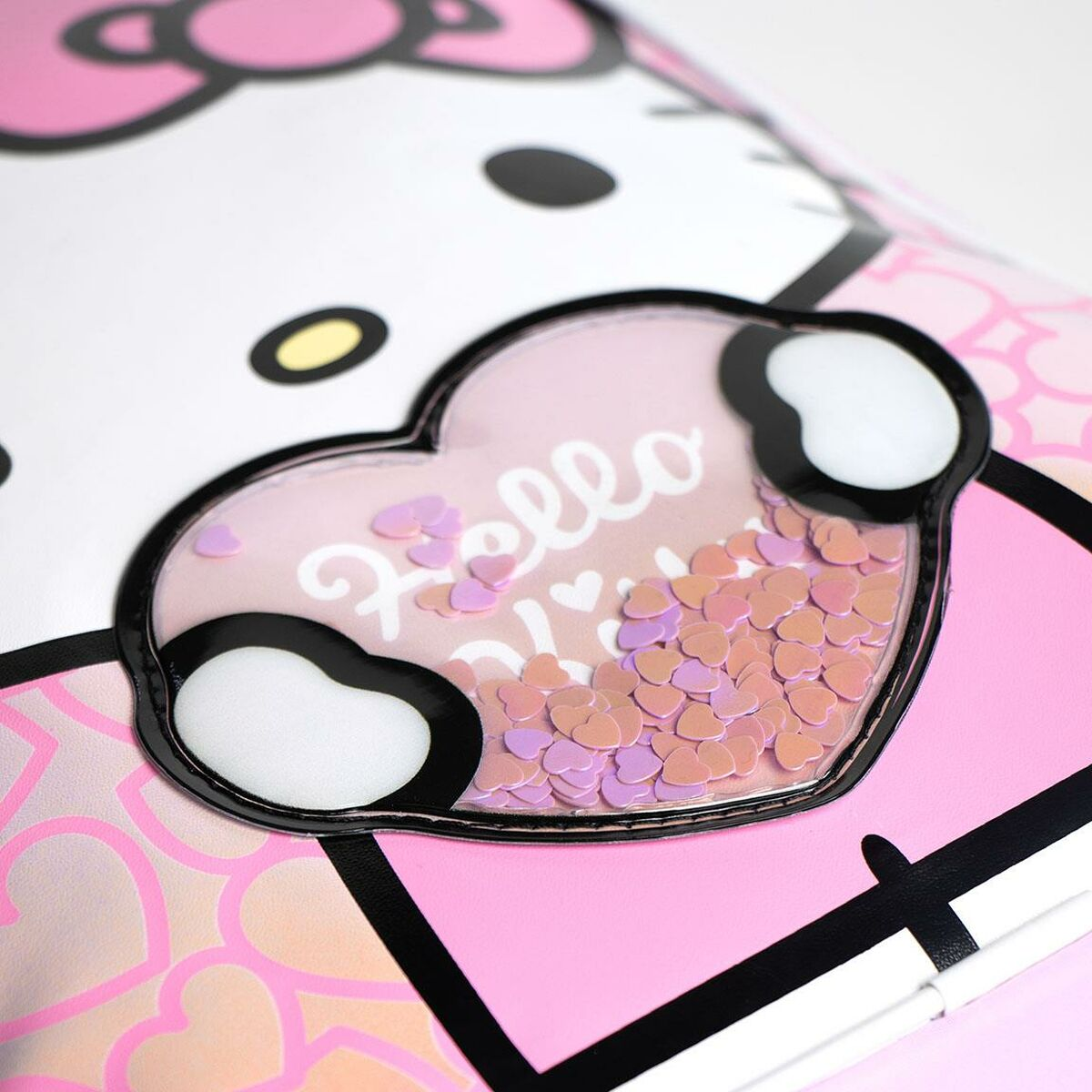 Nahaufnahme einer Hello Kitty-Tasche. Ein herzförmiges Fenster mit 'Hello' und Herzkonfetti. Rosa, Weiß und Schwarz dominieren.