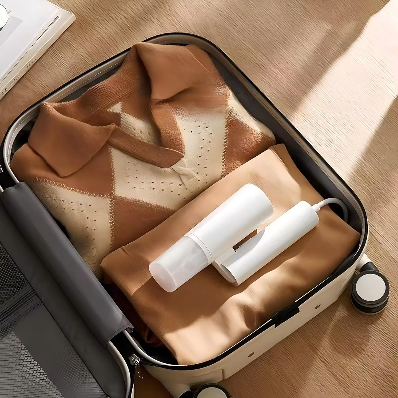 Otwarta walizka, zapakowana w ubrania i białe urządzenie. Beżowe i brązowe ubrania. Jasne drewniane tło podłogi.