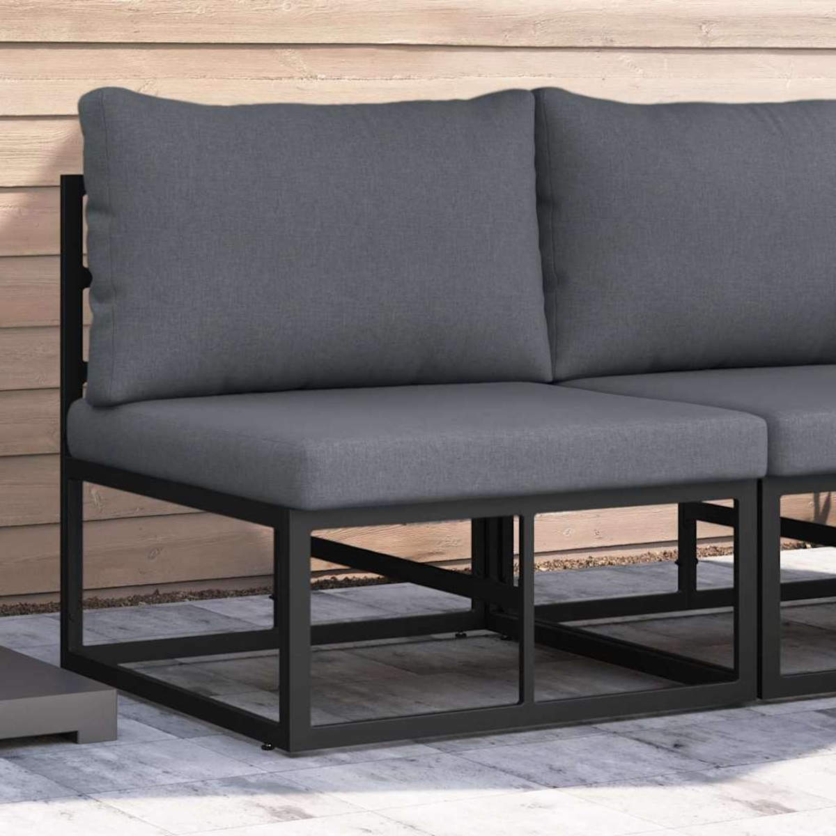 Due sedili imbottiti grigi con telai in metallo nero su un patio grigio. Pannelli di legno sullo sfondo.