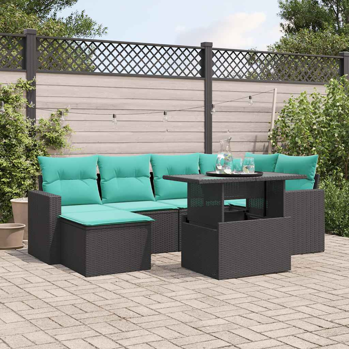 Garten-Set mit grauen Korbmöbeln und türkisfarbenen Kissen, einem Tisch und einem Zaun im Hintergrund.