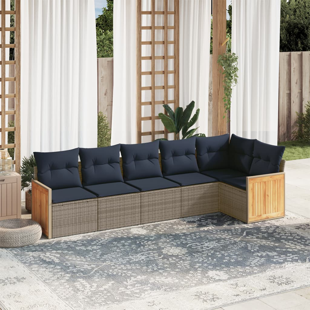 Outdoor-Ecksofa mit marineblauen Kissen. Beiger Rattansockel, Holzakzente und ein gemusterter Teppich. Weiße Vorhänge und Grün im Hintergrund.
