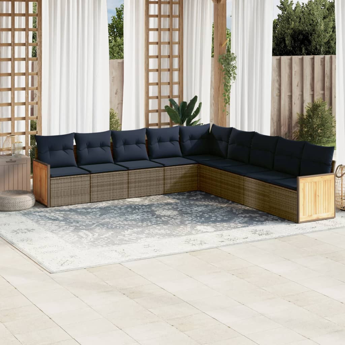Ein Ecksofa im Freien mit marineblauen Kissen steht auf einem gemusterten Teppich. Im Hintergrund befinden sich weiße Vorhänge und Holzstrukturen.