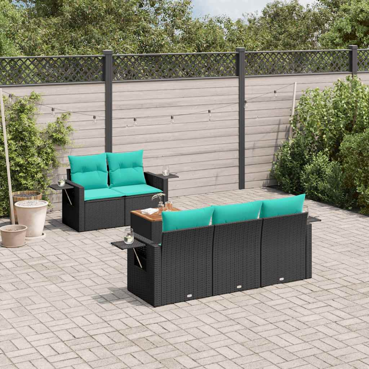 Juego de muebles de patio: sofás de mimbre negro con cojines turquesa, mesa pequeña. Fondo: valla de madera, vegetación, patio de ladrillos.