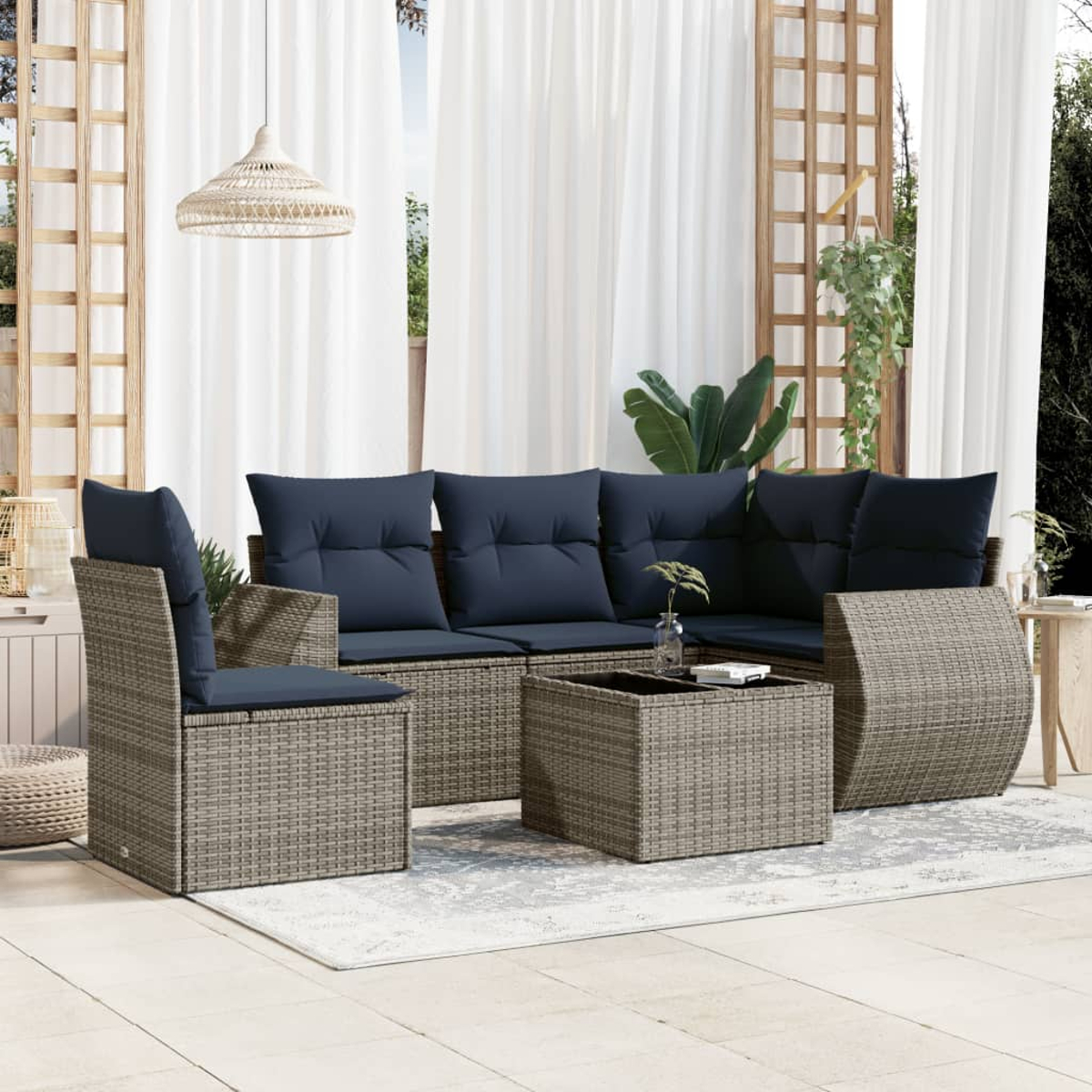 Outdoor-Rattansofa-Set mit marineblauen Kissen. Inklusive Couchtisch. Auf einer Terrasse mit weißen Vorhängen und einer Hängelampe.