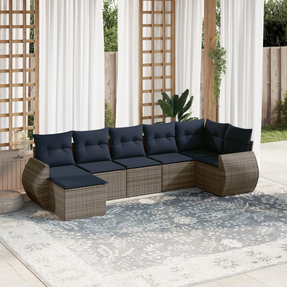 Ein Ecksofa im Freien mit blauen Kissen auf einem gemusterten Teppich. Weiße Vorhänge und Holzgitter im Hintergrund.